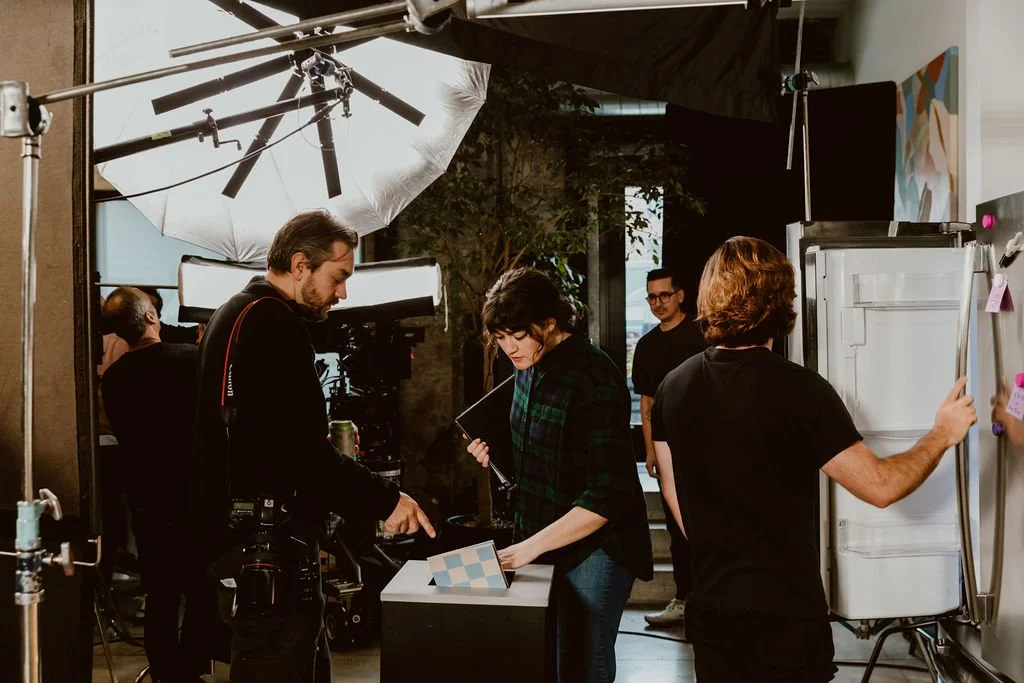 A film crew working in a studio, with a woman reviewing a stand-up and a man adjusting a whiteboard.