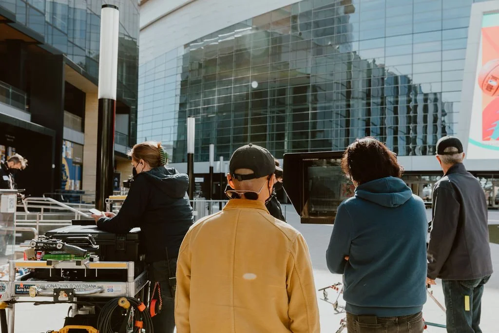 Filmmakers and crew setting up equipment outdoors in front of a modern glass building during the daytime.