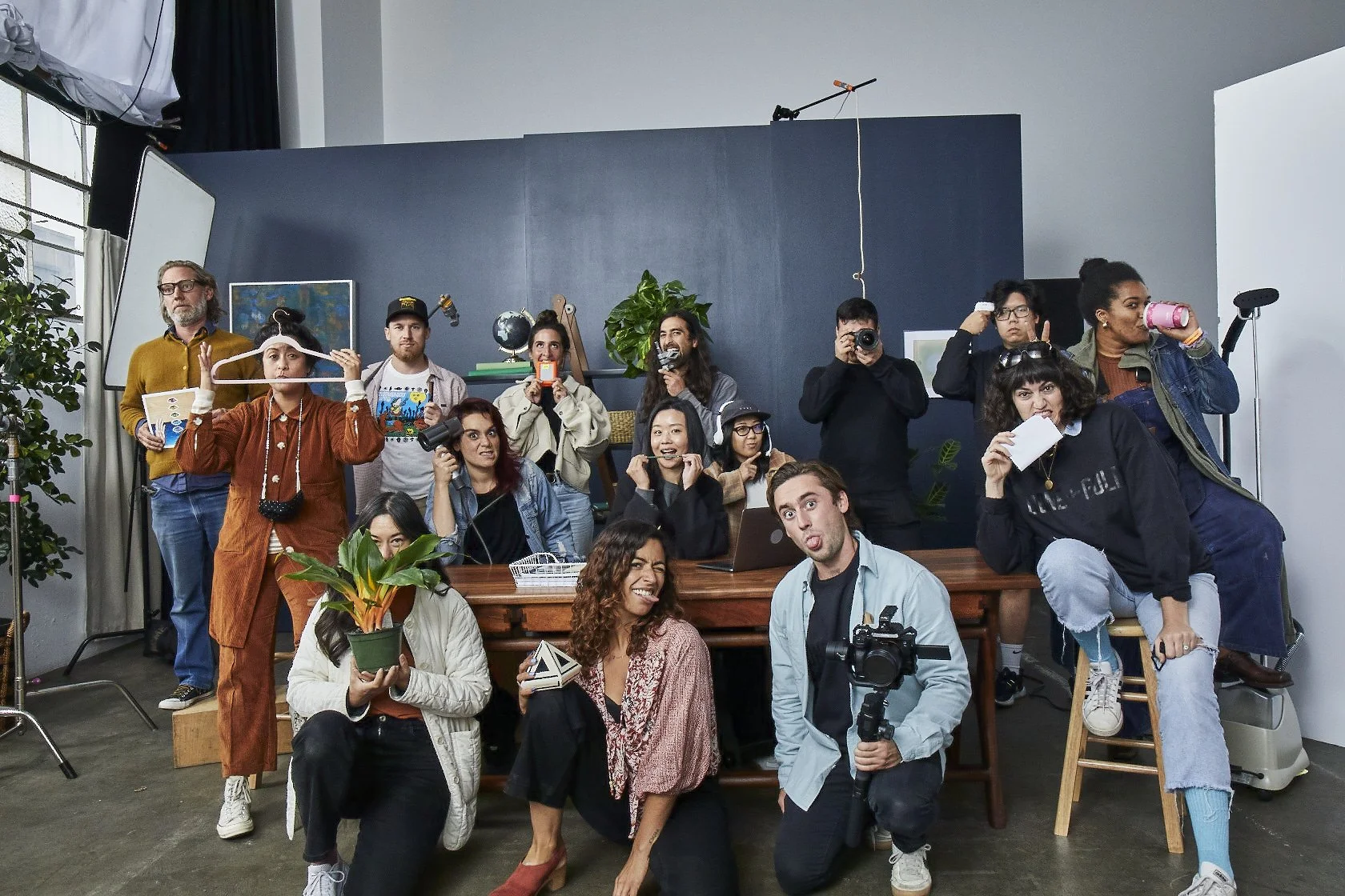 Group of people posing and making funny faces in a modern studio setting with equipment, plants, and a blue wall.