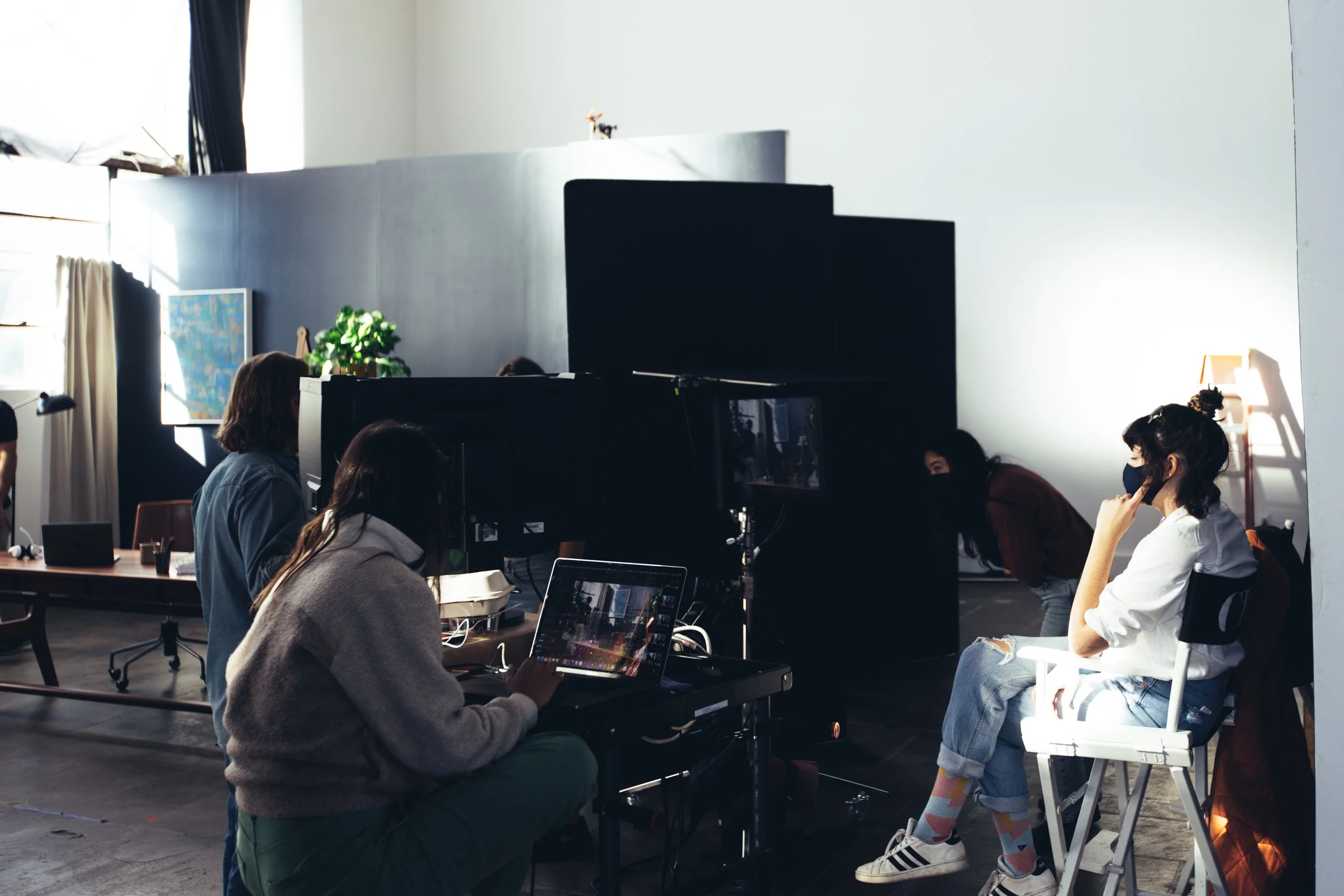 People working on laptops in a bright workspace with large windows, a mirror, and a small plant.