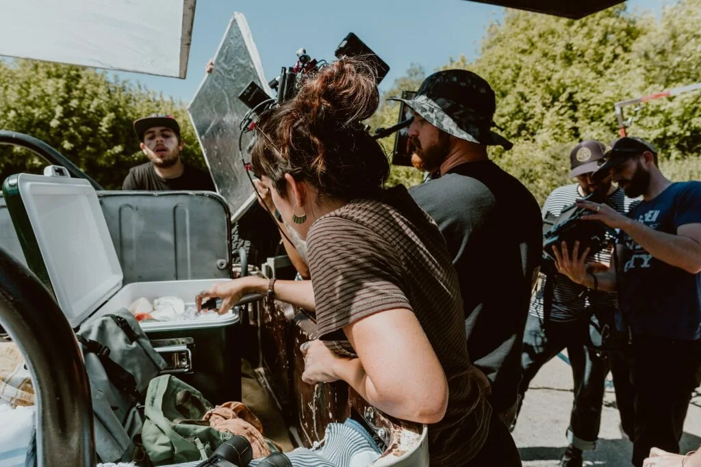 Crew members preparing equipment on a film set outdoors with green trees in the background.