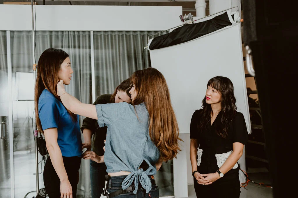 A woman in blue being prepared for a photo shoot by a team of makeup artists and stylists in a studio.