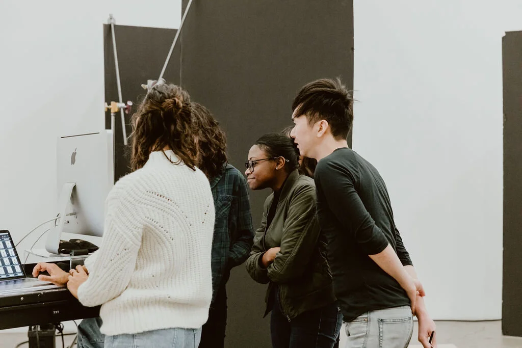 Group of four people, two women and two men, gathered around a computer monitor in a modern studio with black and white walls.