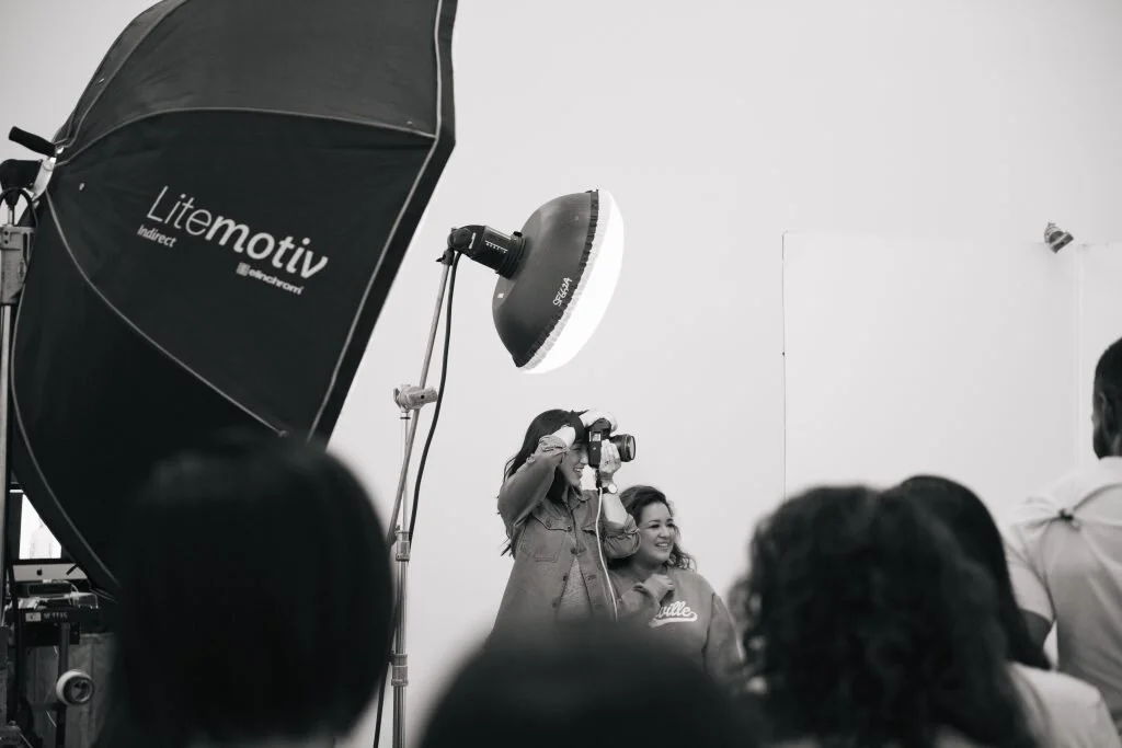 Photographer taking a picture of smiling woman at a photography event with studio lights and umbrellas.