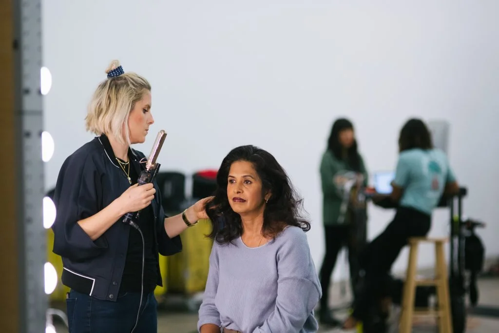 Makeup artist applying makeup to a woman sitting in a salon or studio setting.