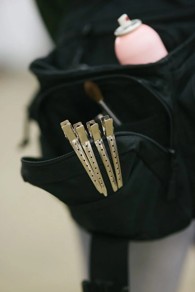 A black backpack with a zipper pocket containing five metal lockpicks and a pink spray can with a white cap.