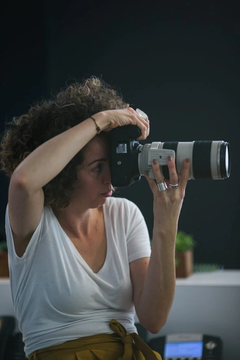 A woman with curly hair taking a photograph with a professional camera indoors.