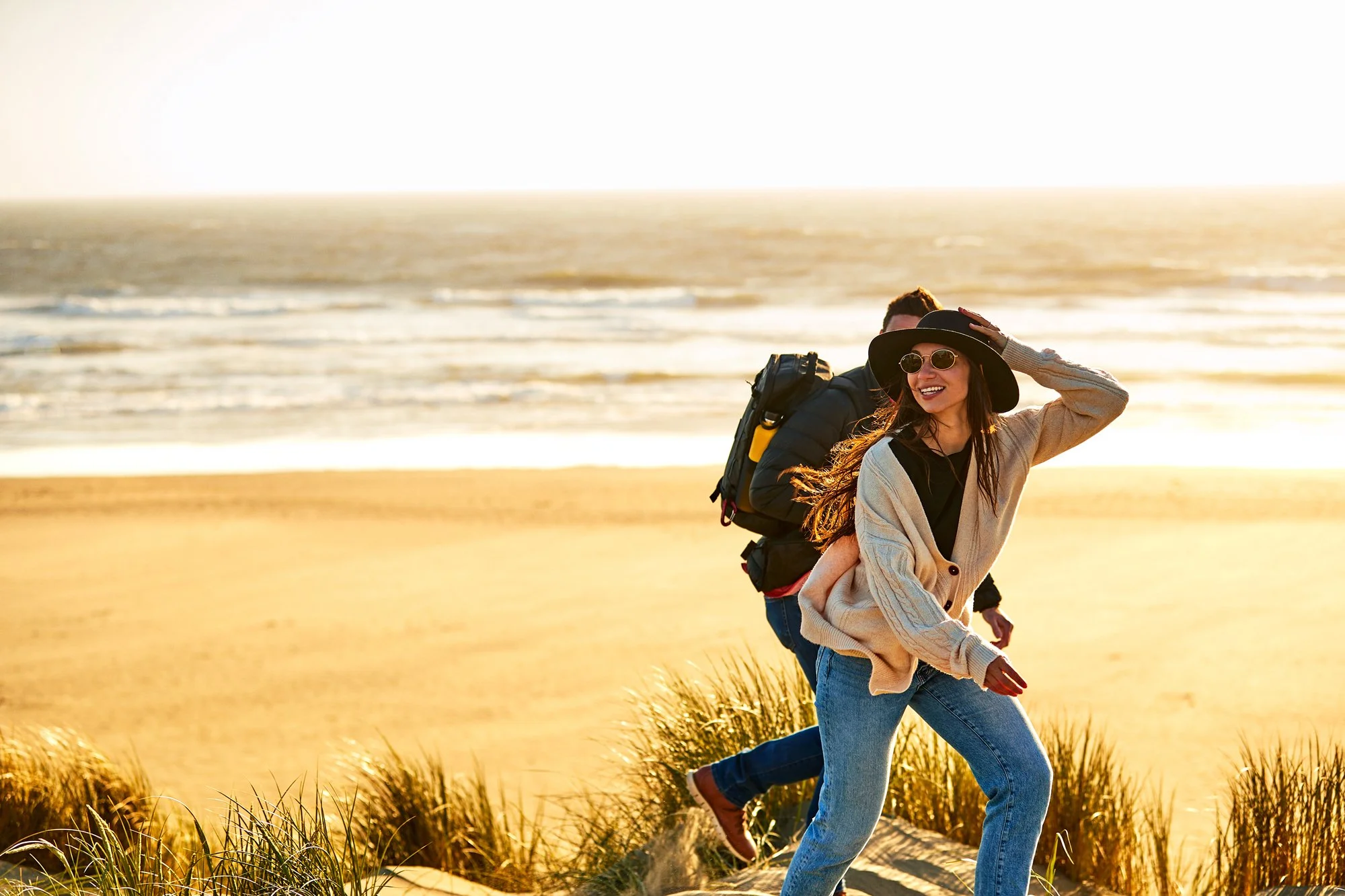 Two women and a man walking on a beach at sunset, smiling and enjoying the outdoors, with the ocean in the background.