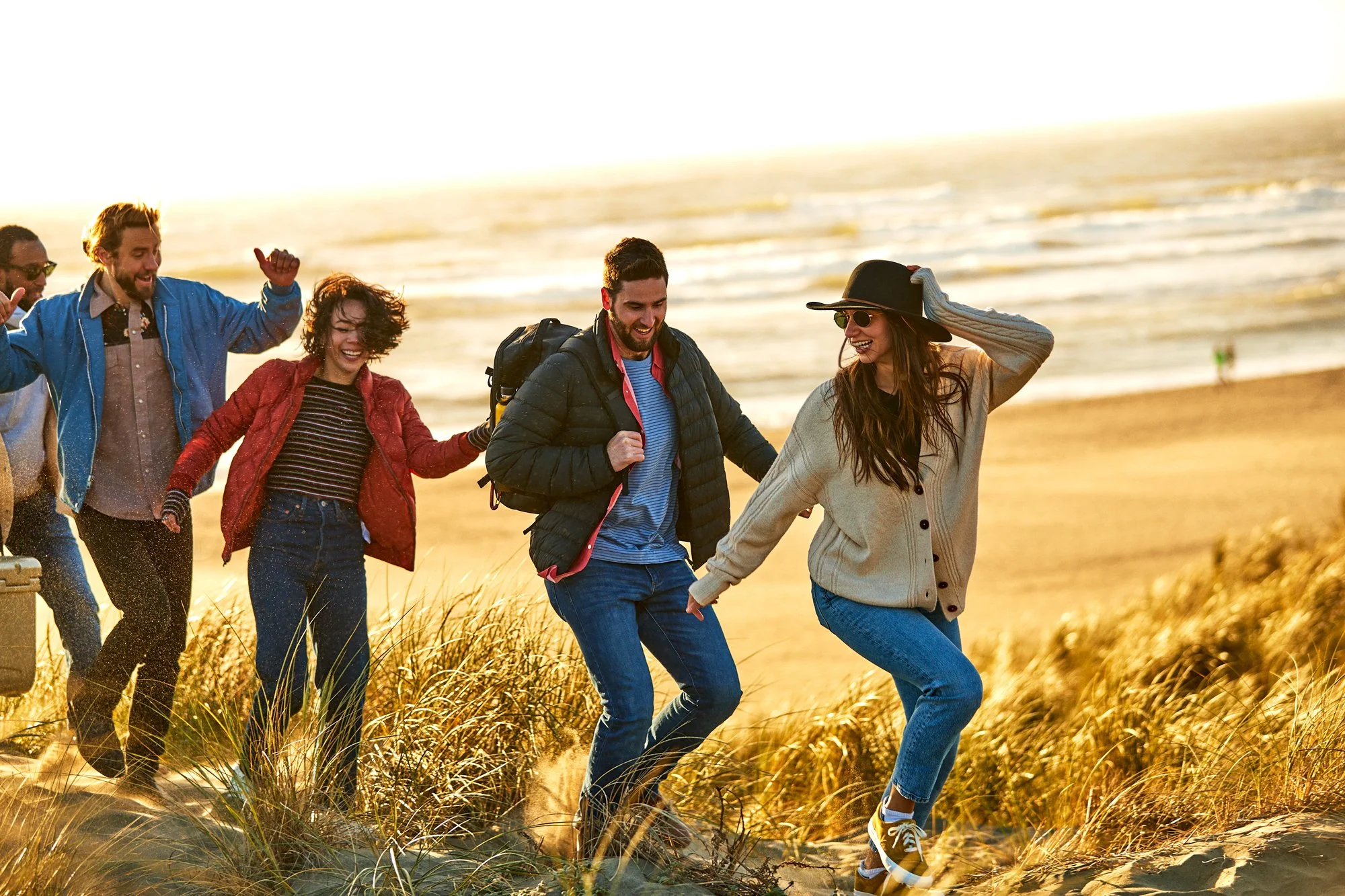A group of friends walking on a beach at sunset, smiling and enjoying the outdoor scenery.