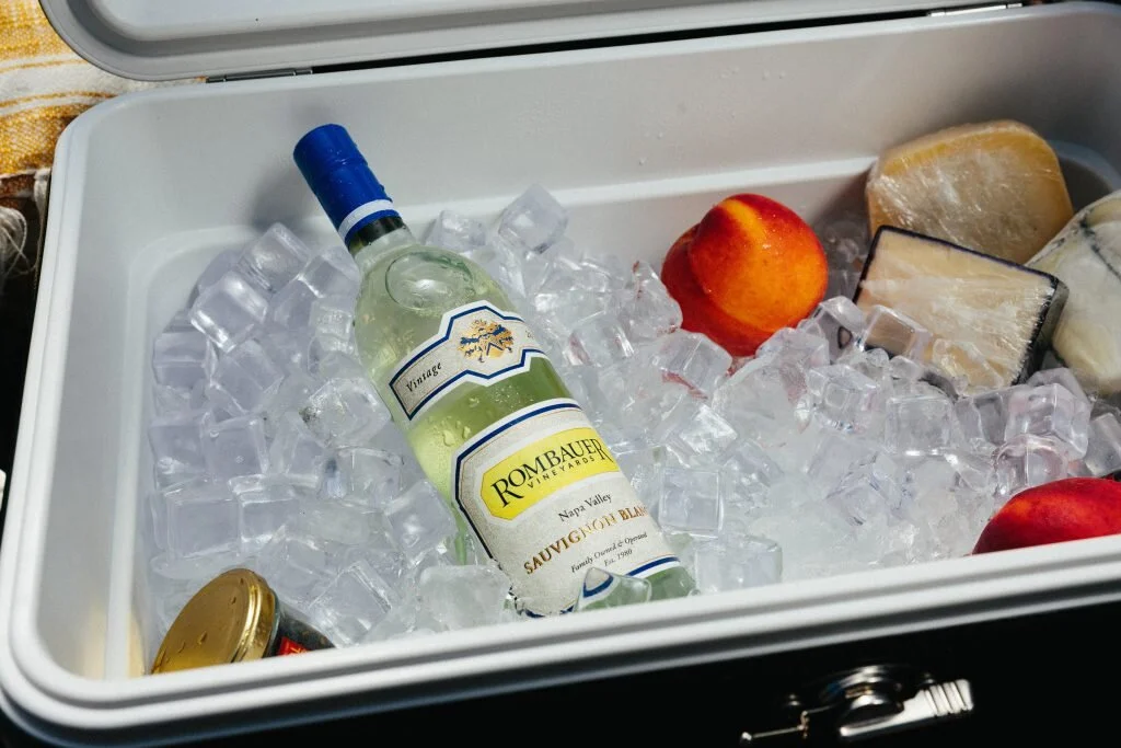 A cooler filled with ice, a bottle of wine, peaches, and cheese.