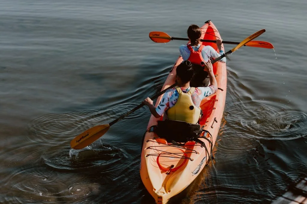 Three people kayaking on a calm body of water, with paddles in motion.