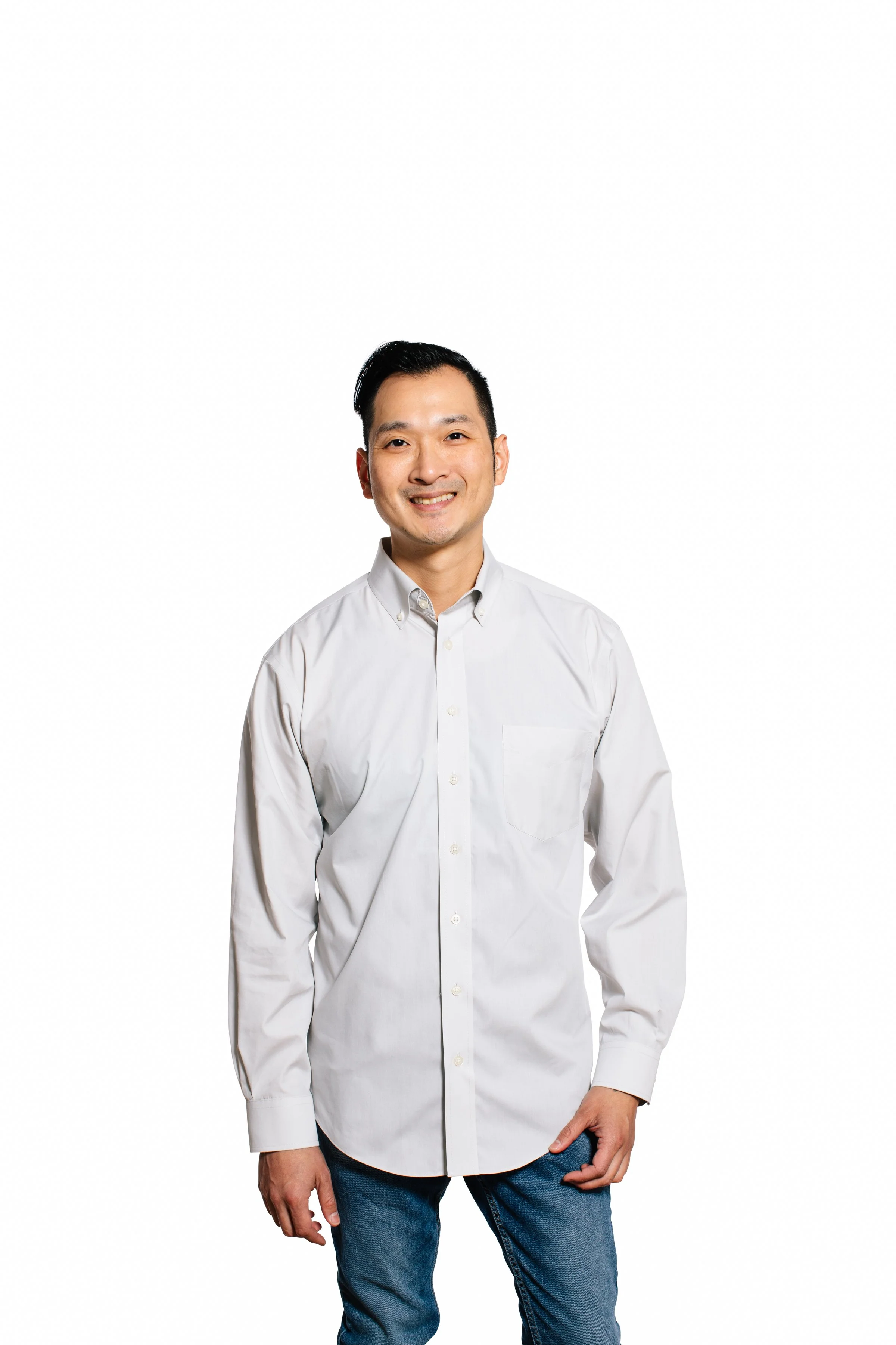A smiling man in a white button-up shirt and blue jeans standing against a plain white background.
