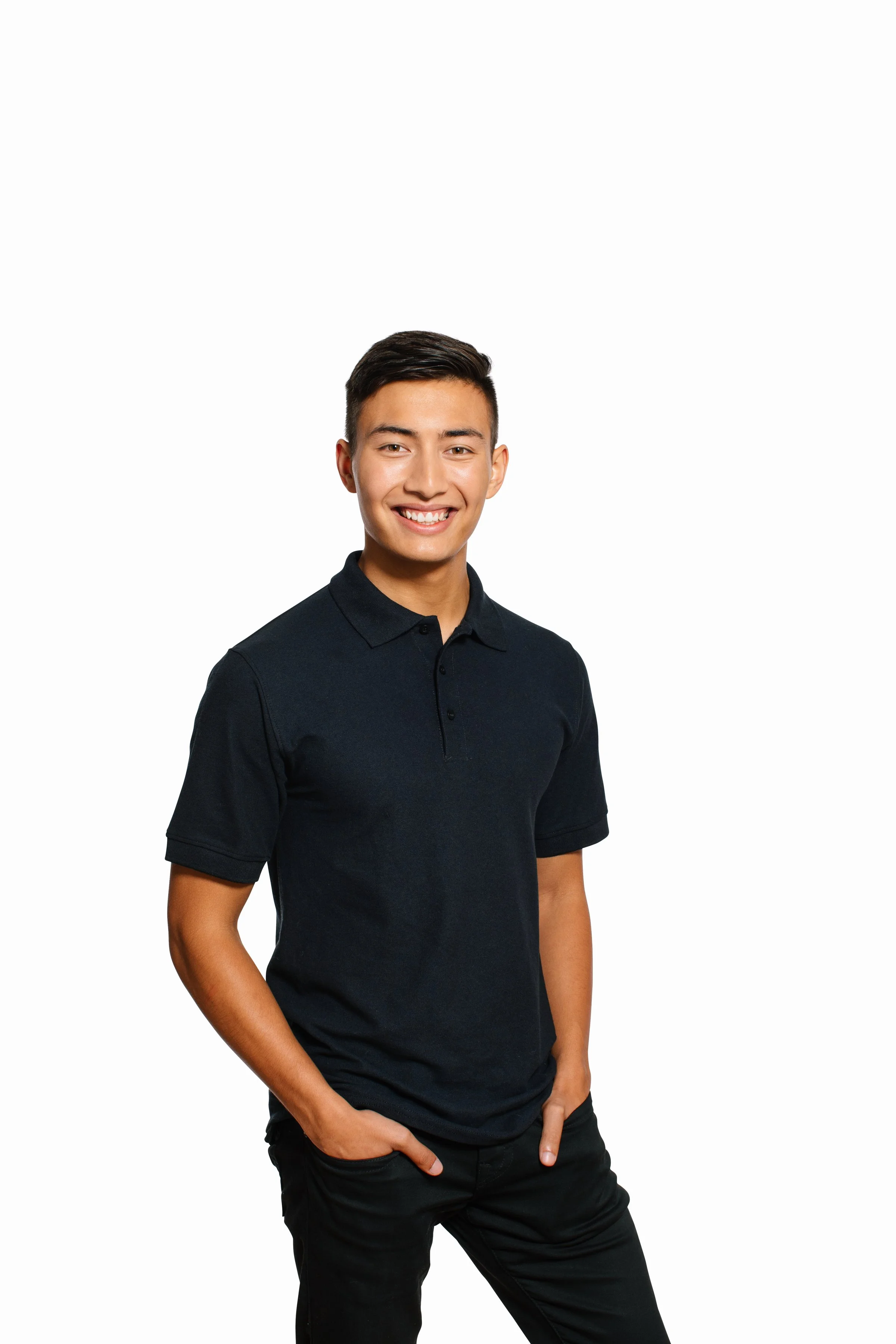 Young man with short dark hair, smiling, wearing a black polo shirt and black pants, standing with hand in pocket against a plain white background.