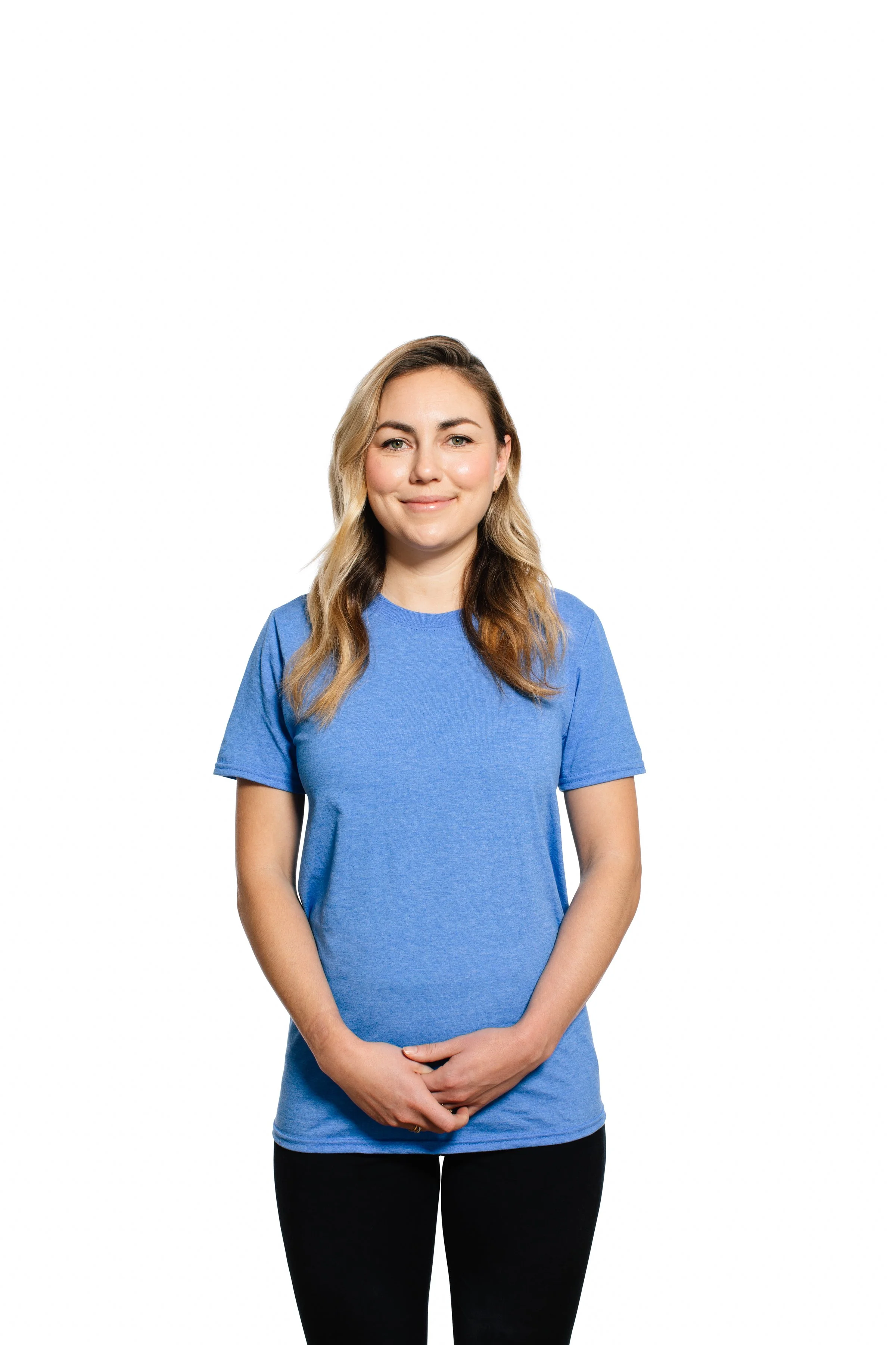 A young woman with long, wavy blonde hair, wearing a blue t-shirt, smiling softly with clasped hands against a plain white background.
