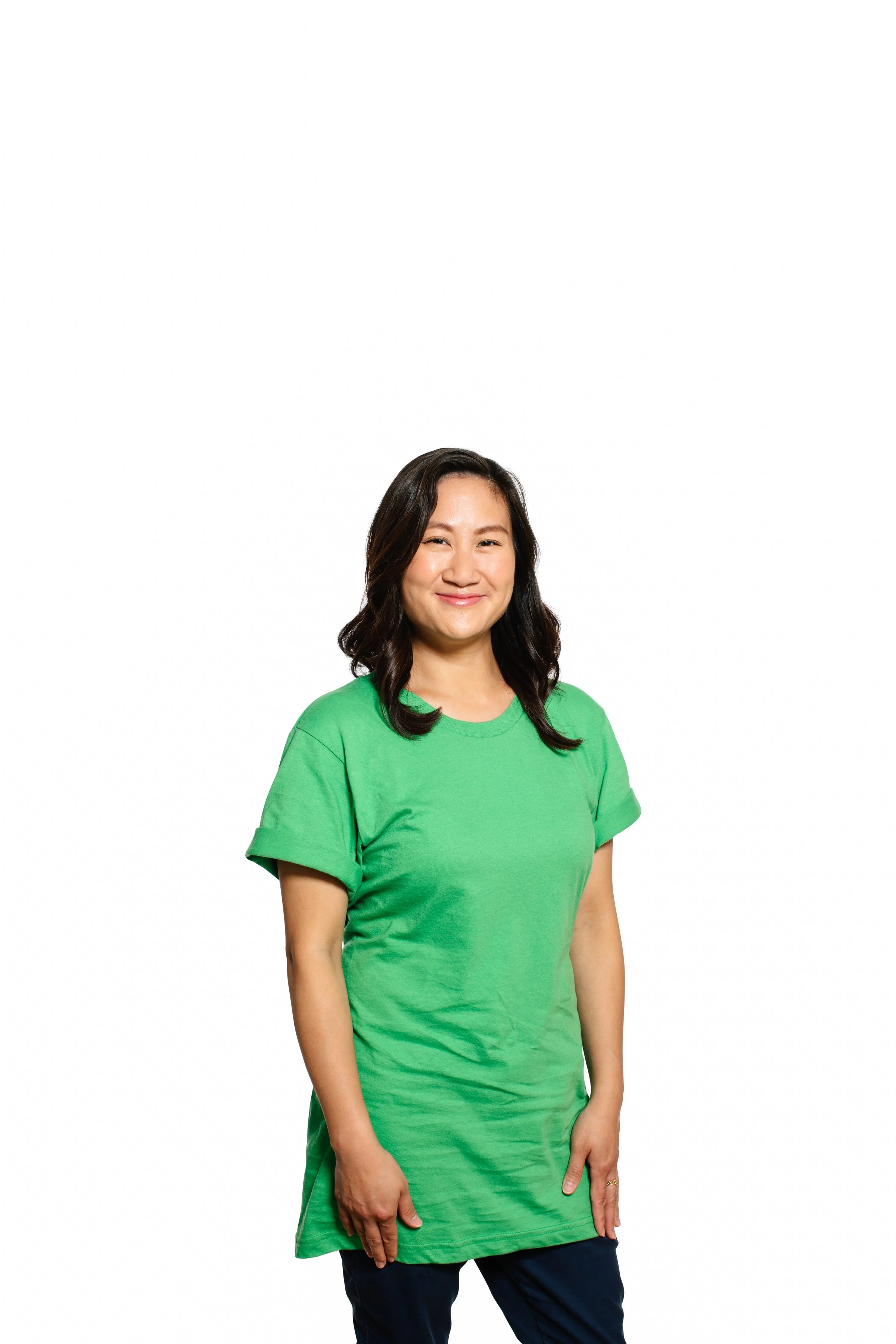 A woman wearing a green T-shirt and navy pants smiling against a plain white background.