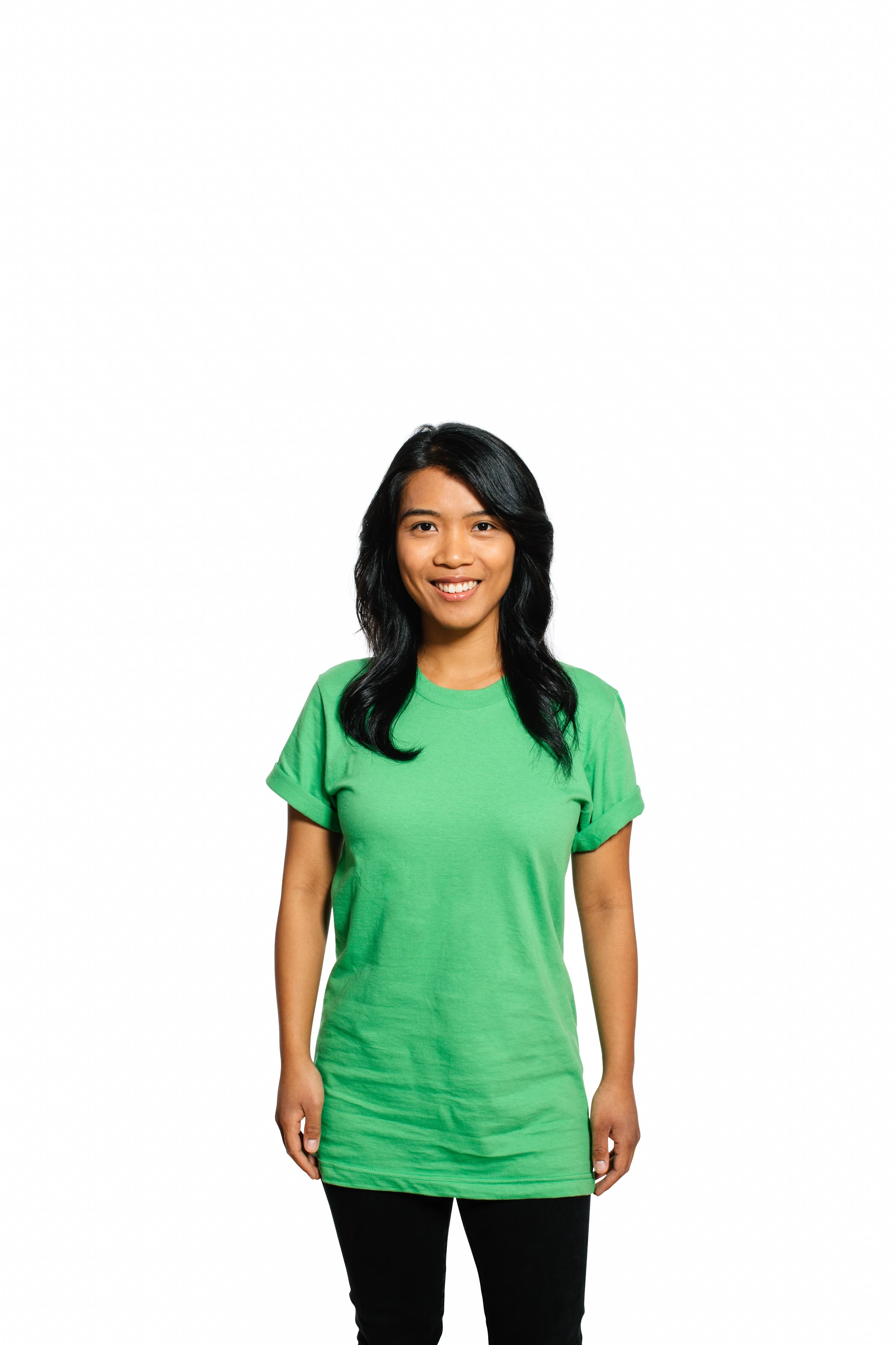 Young woman with long black hair smiling, wearing a green dress and black pants, standing against a white background.