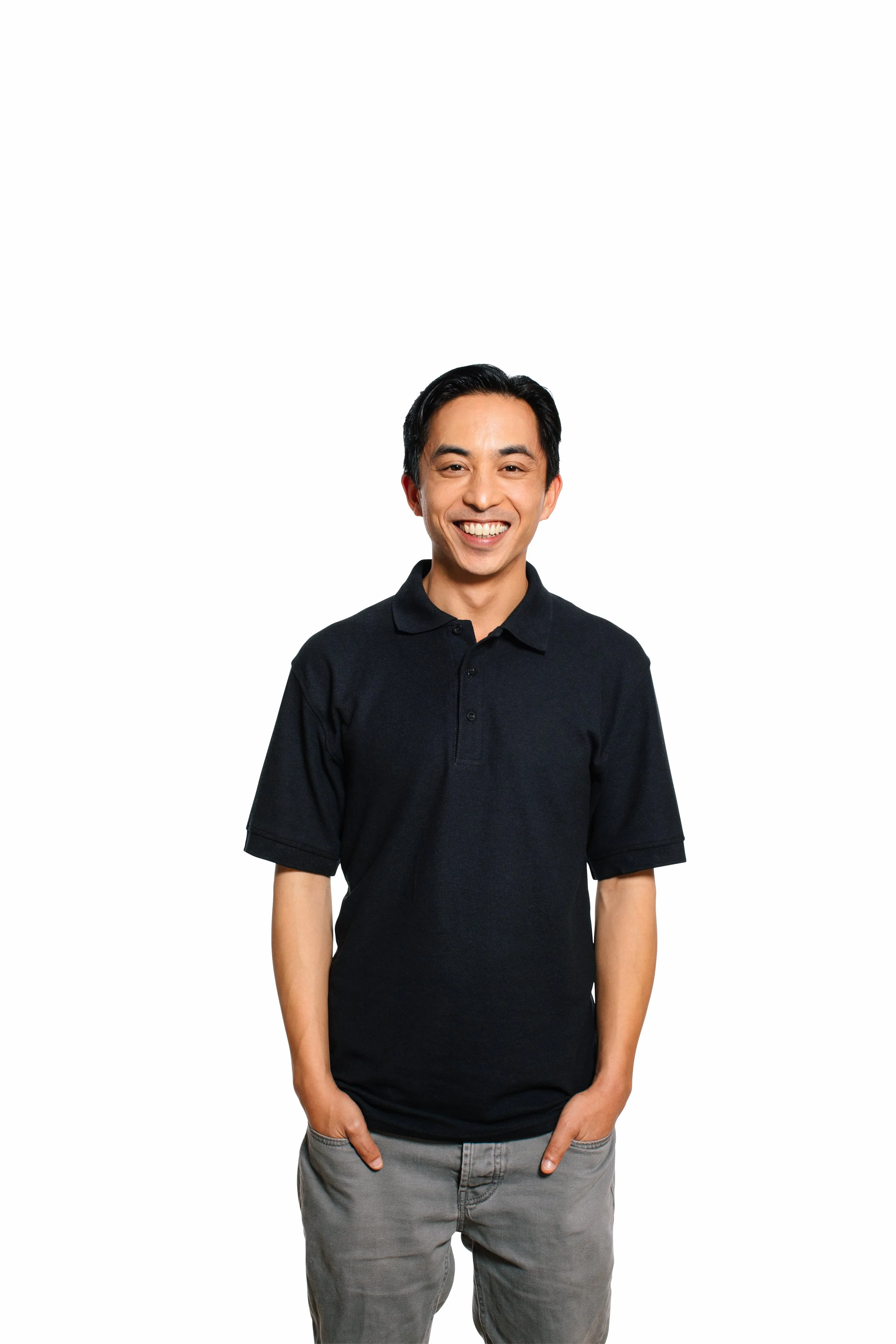 A young man with short black hair, smiling, wearing a black polo shirt and gray pants, standing against a white background.