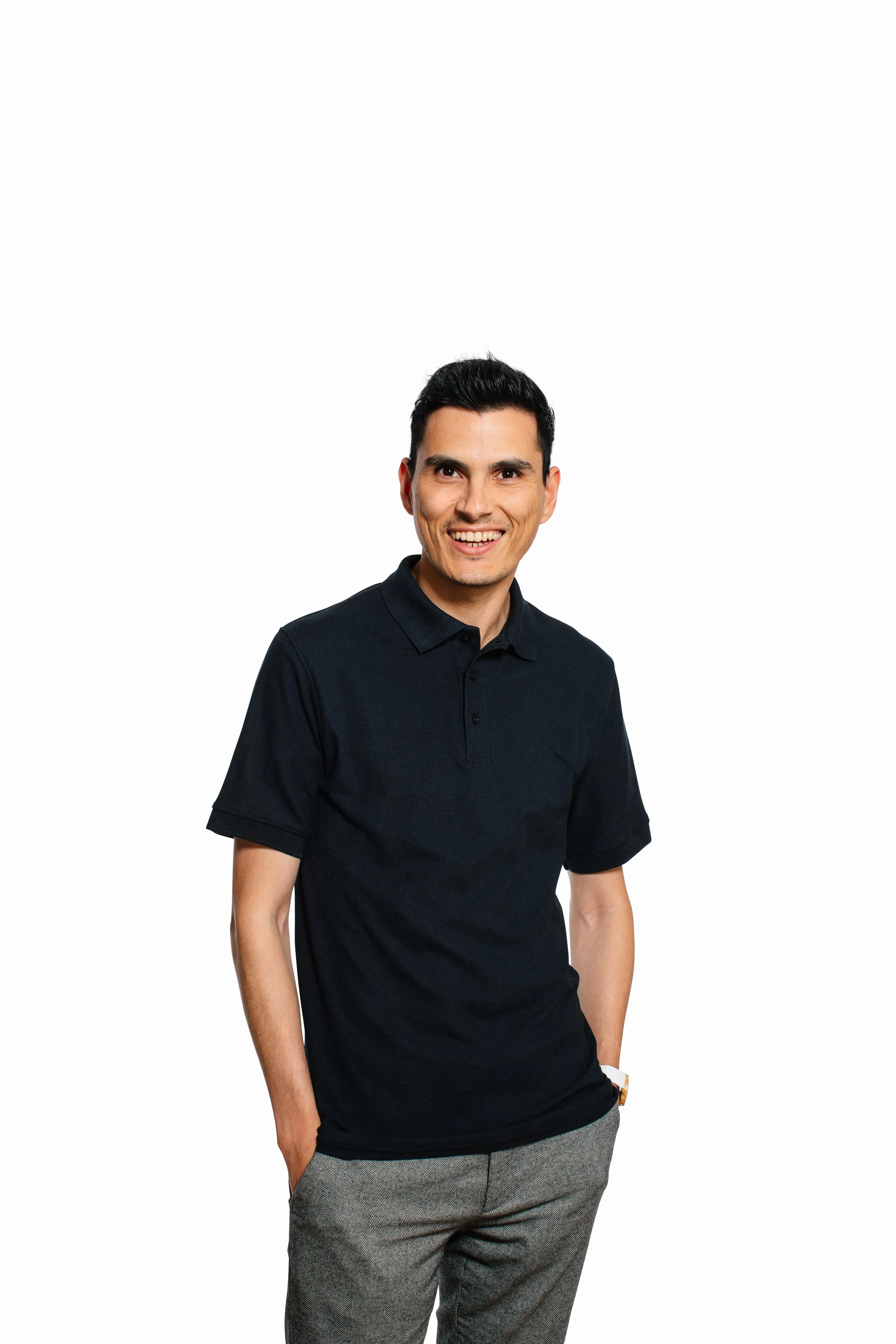 A man standing with his left hand in his pocket, wearing a black polo shirt and gray plaid trousers, smiling and looking at the camera against a plain white background.