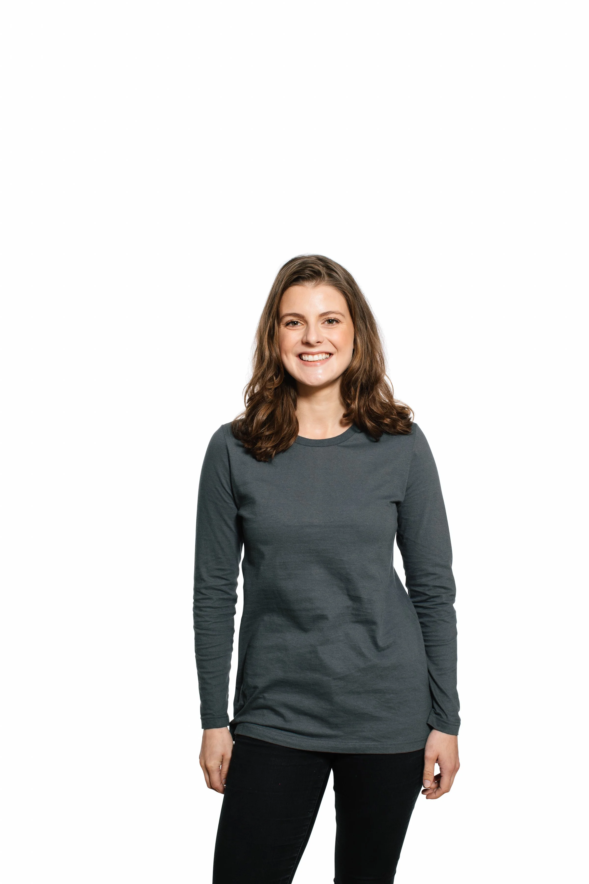 A woman with brown hair smiling, wearing a dark gray long-sleeve shirt and black pants, standing against a plain white background.