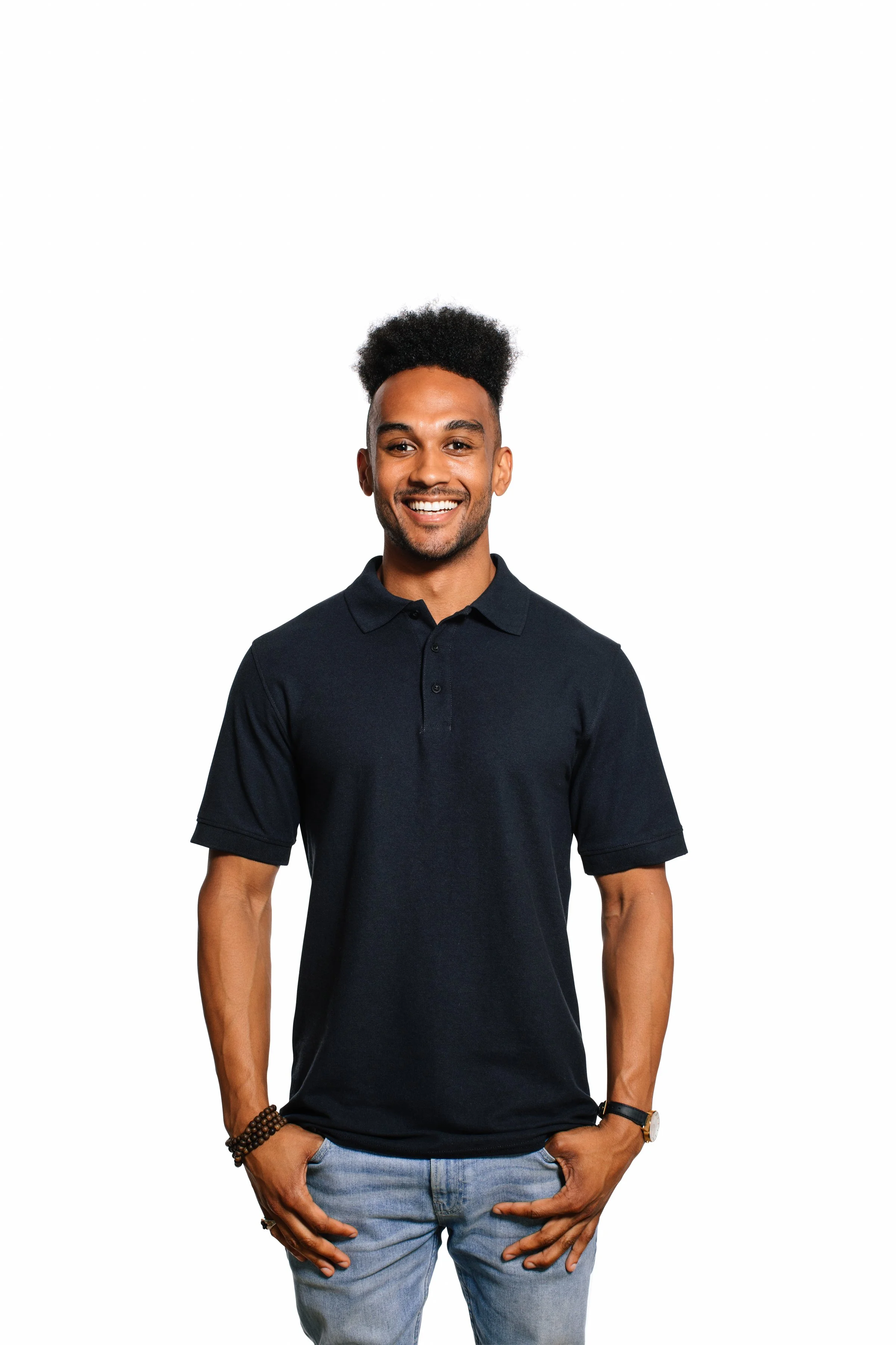 A smiling man with short black hair, wearing a dark polo shirt and light blue jeans, standing against a plain white background.