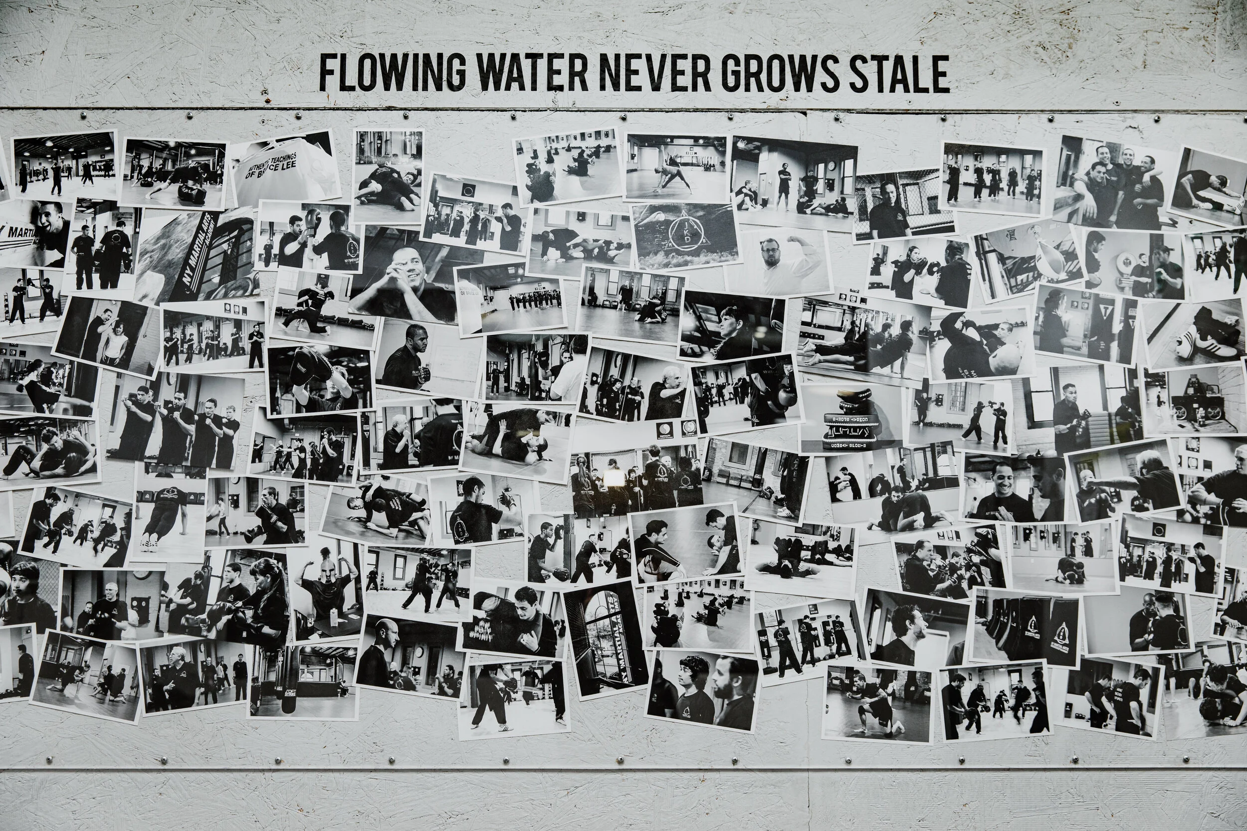 A wall with a collage of black-and-white photographs of people practicing martial arts and training in a gym. Above the photos, a sign reads "Flowing water never grows stale."
