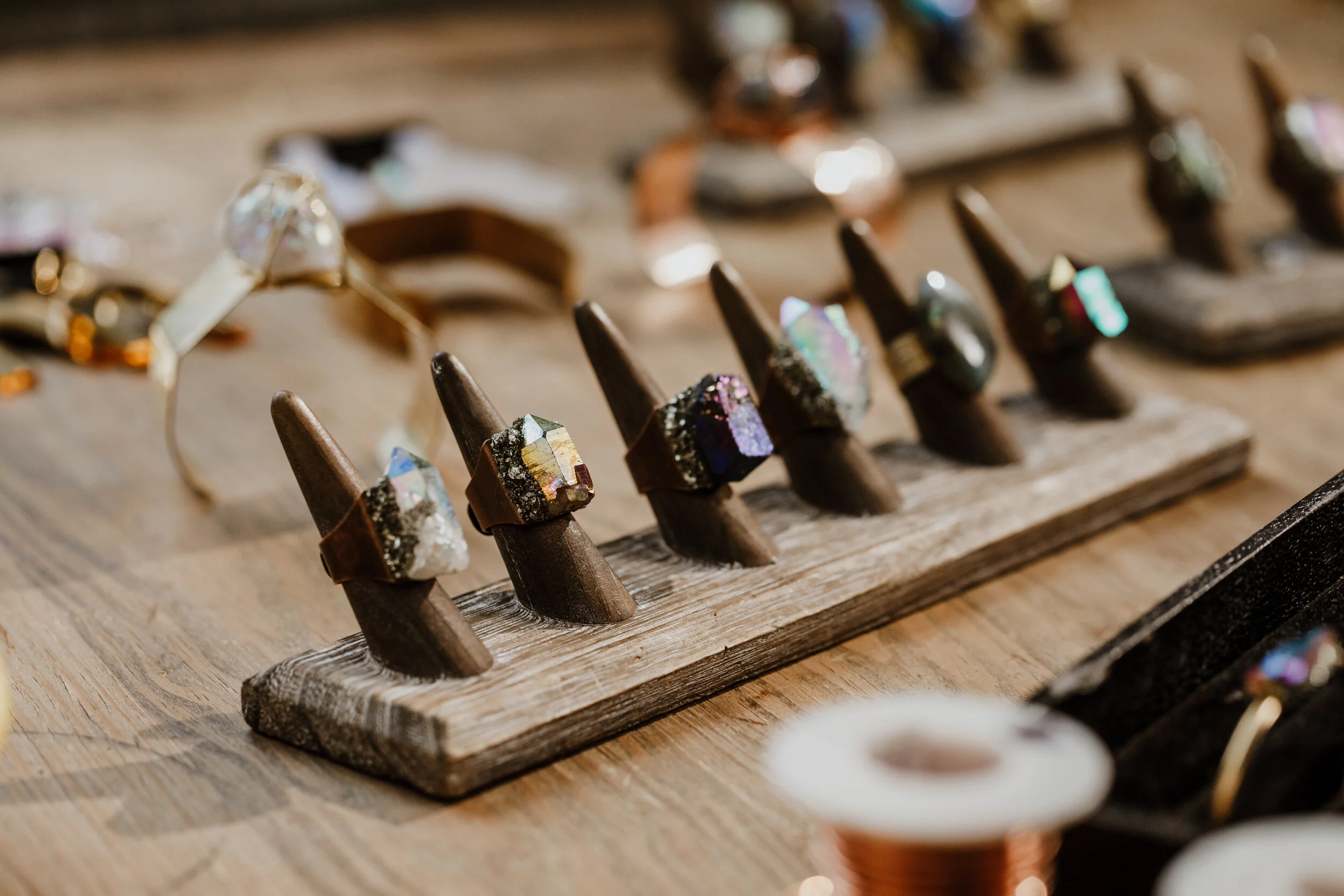 Close-up of a wooden display stand with several rings featuring large, colorful gemstone-like stones.