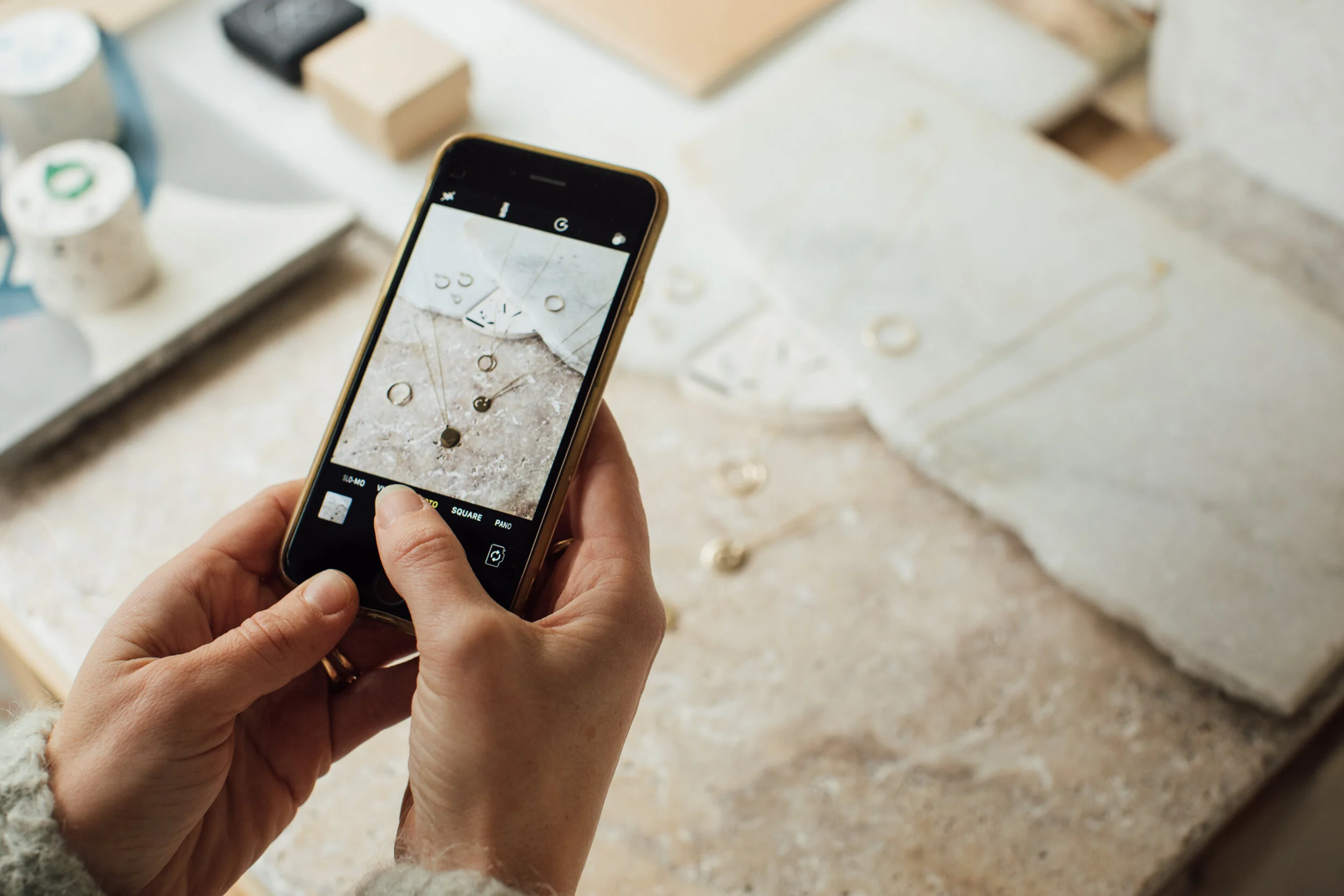 Person taking a photo of small metallic objects, possibly jewelry, on a surface using a smartphone.