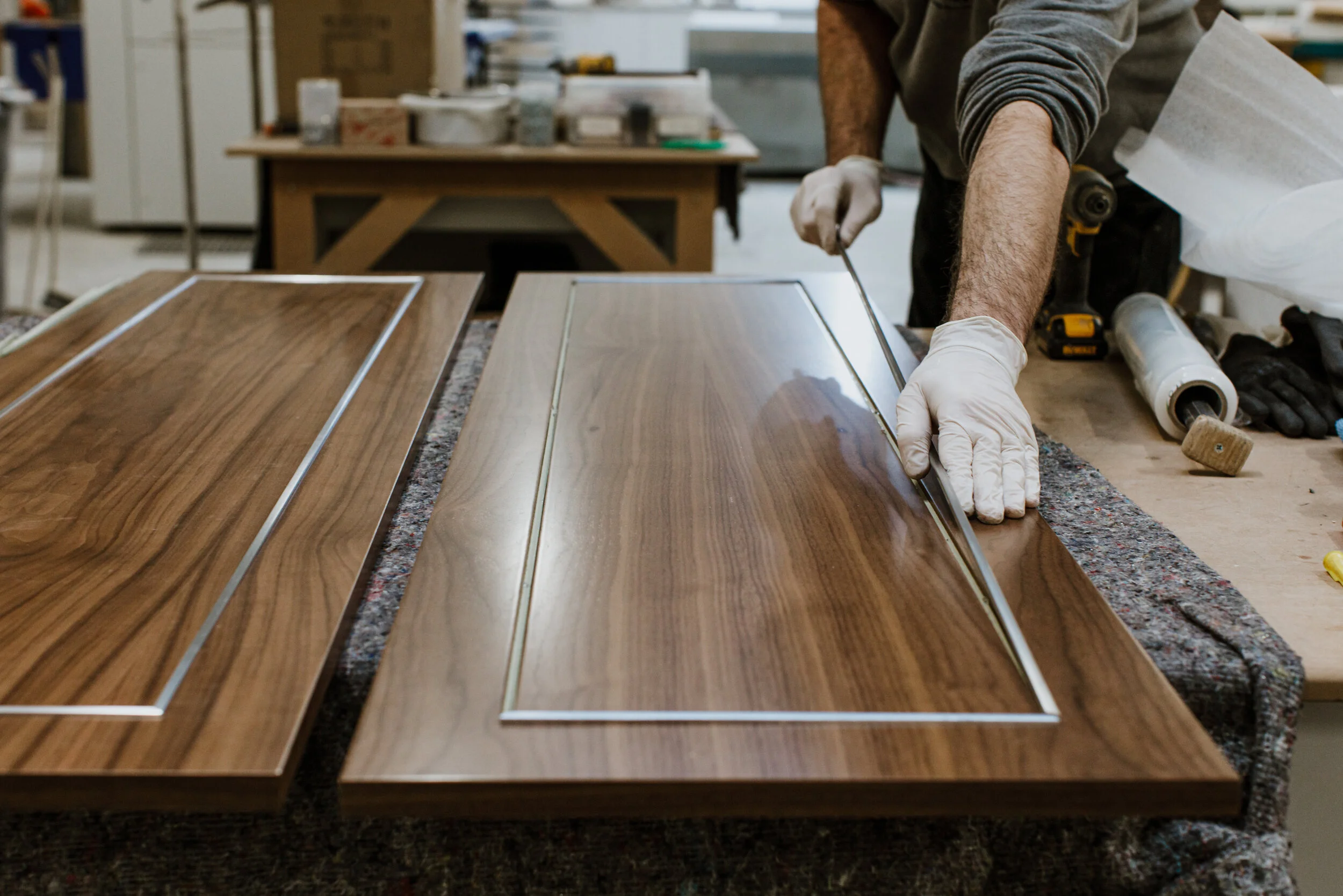 A person working on a woodworking project at a workbench in a workshop, assembling or finishing a piece of polished wood furniture.