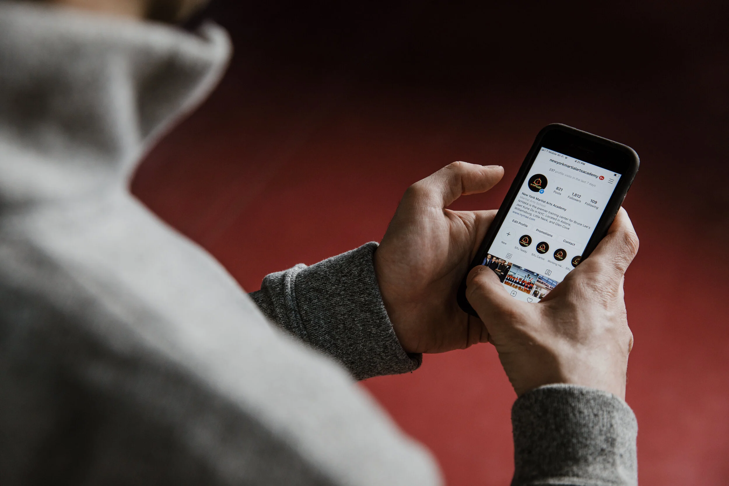 Person holding a smartphone, viewing a social media profile with a martial arts school location and details.