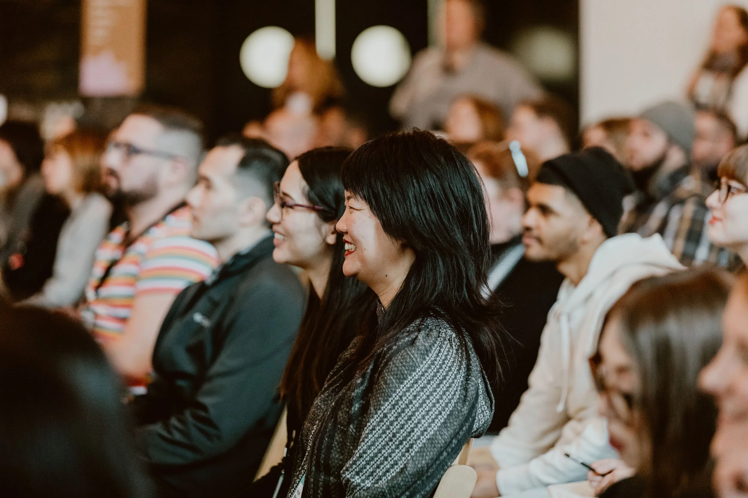 People attending a conference or seminar, seated and listening attentively, with some smiling.