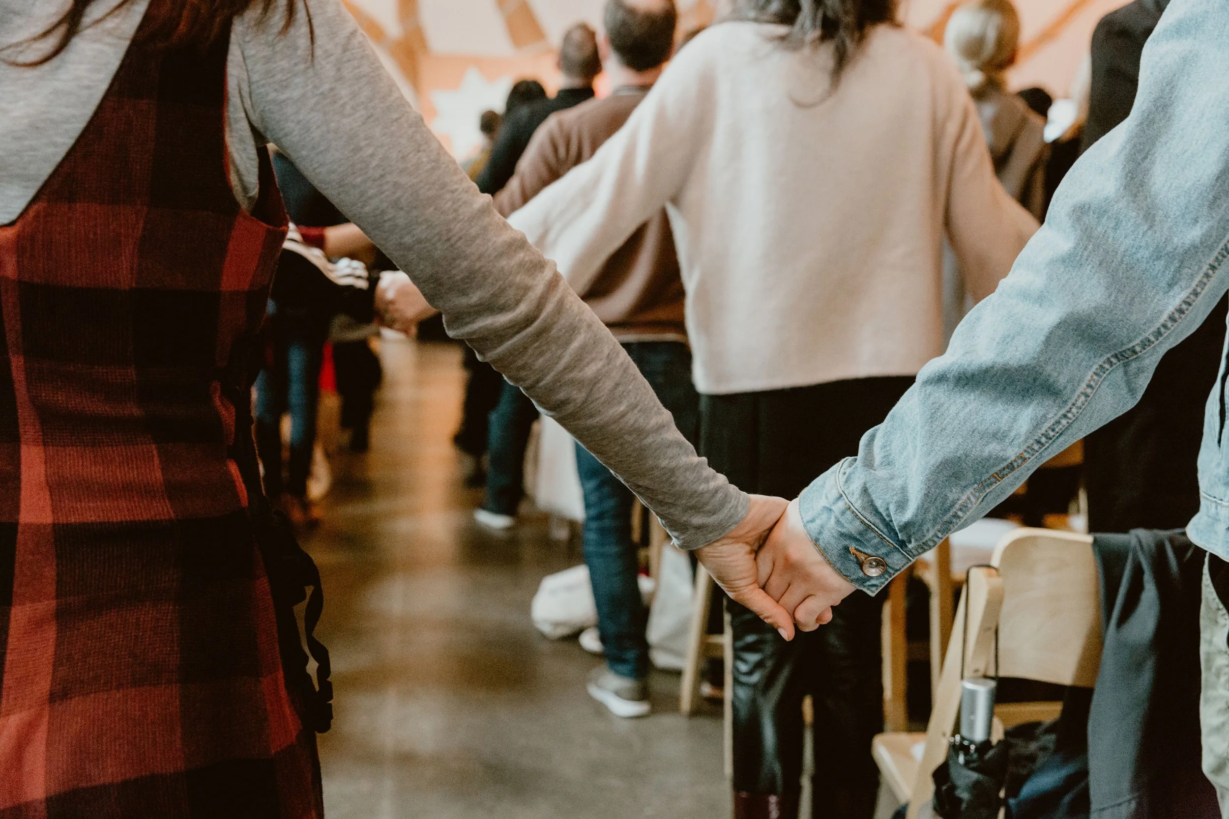 People holding hands in a line, participating in a group activity or ceremony indoors.