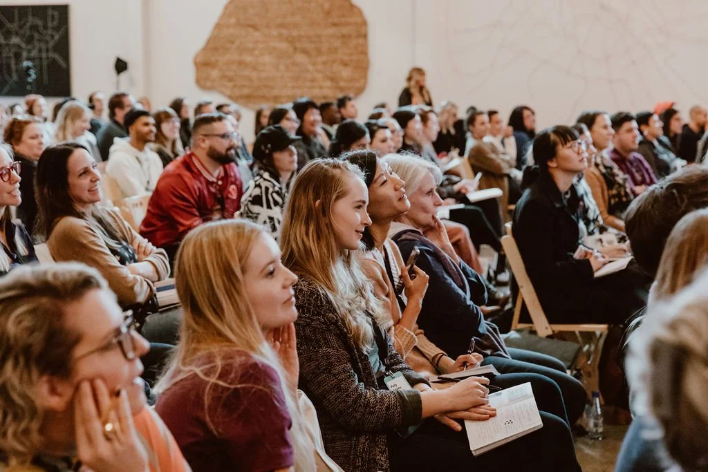 A large group of people attending a conference or seminar indoors, sitting and listening attentively.