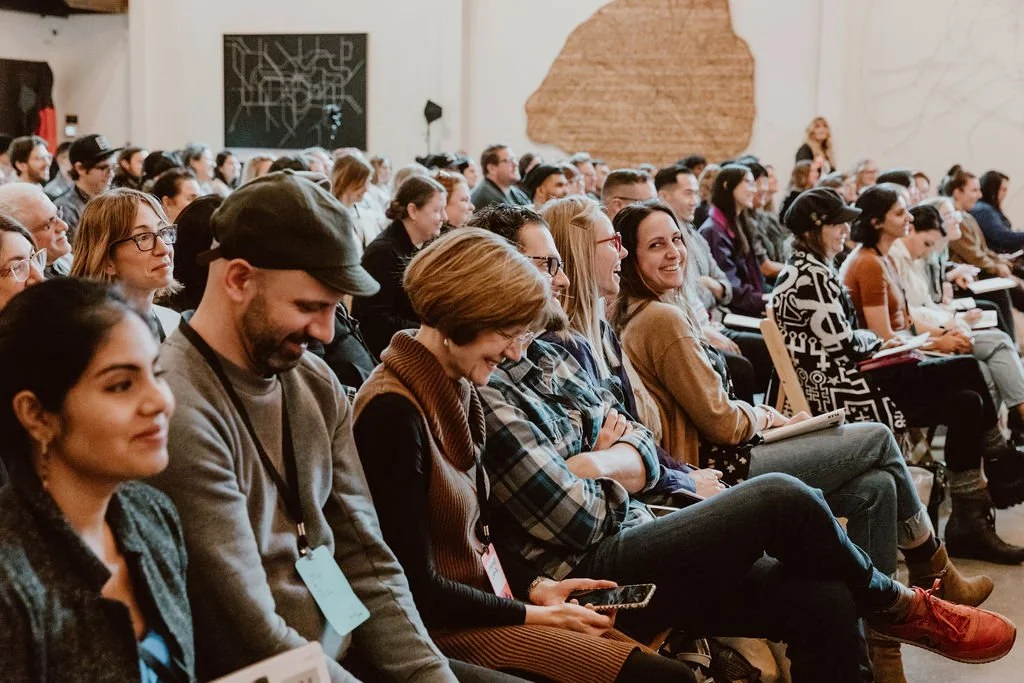 Audience seated in a conference room, paying attention and smiling.