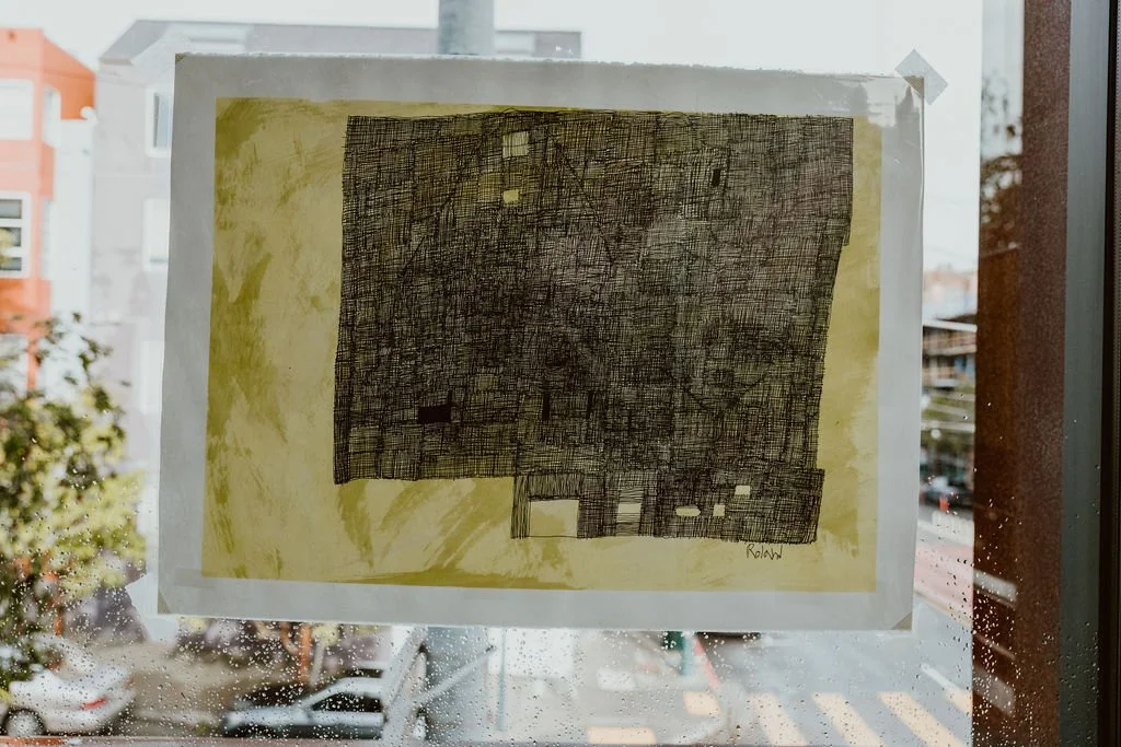 Abstract black and yellow drawing of a building plan or city map on paper tacked to a window with rainy street scene outside.