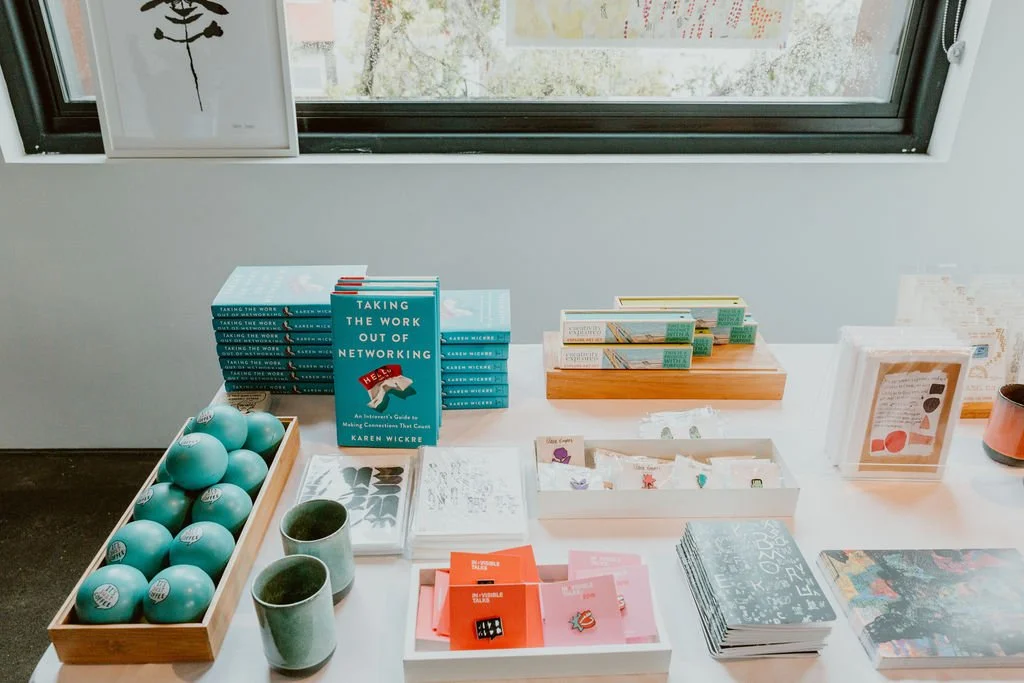 Books about networking and communication on a table, alongside teal-colored mugs and balls, with artwork and a window in the background.