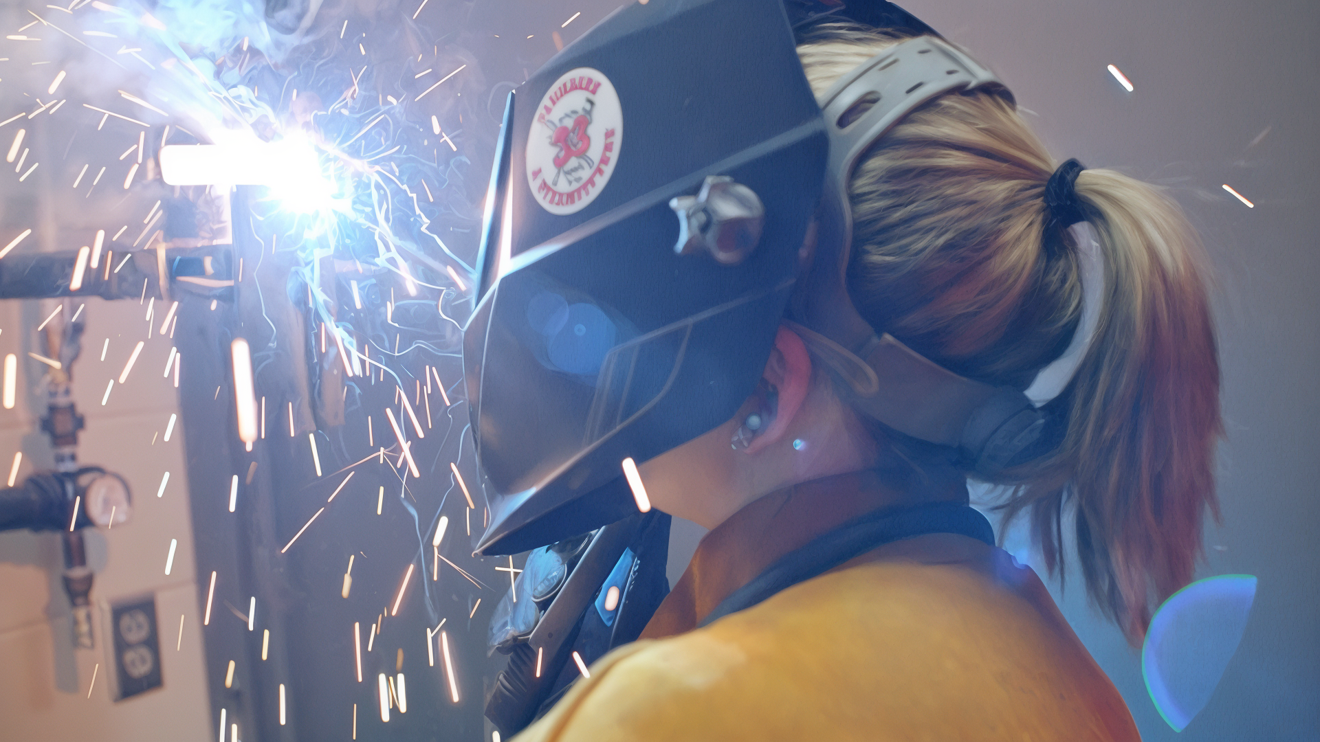 Person welding with protective gear, sparks flying in the workspace.