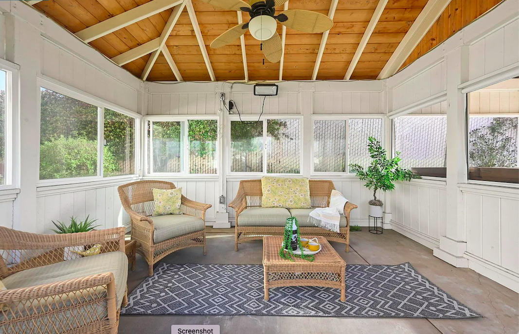 Sunroom with wicker furniture, including a loveseat and two armchairs with cushions, a woven coffee table with a tray, potted plants, and a ceiling fan.