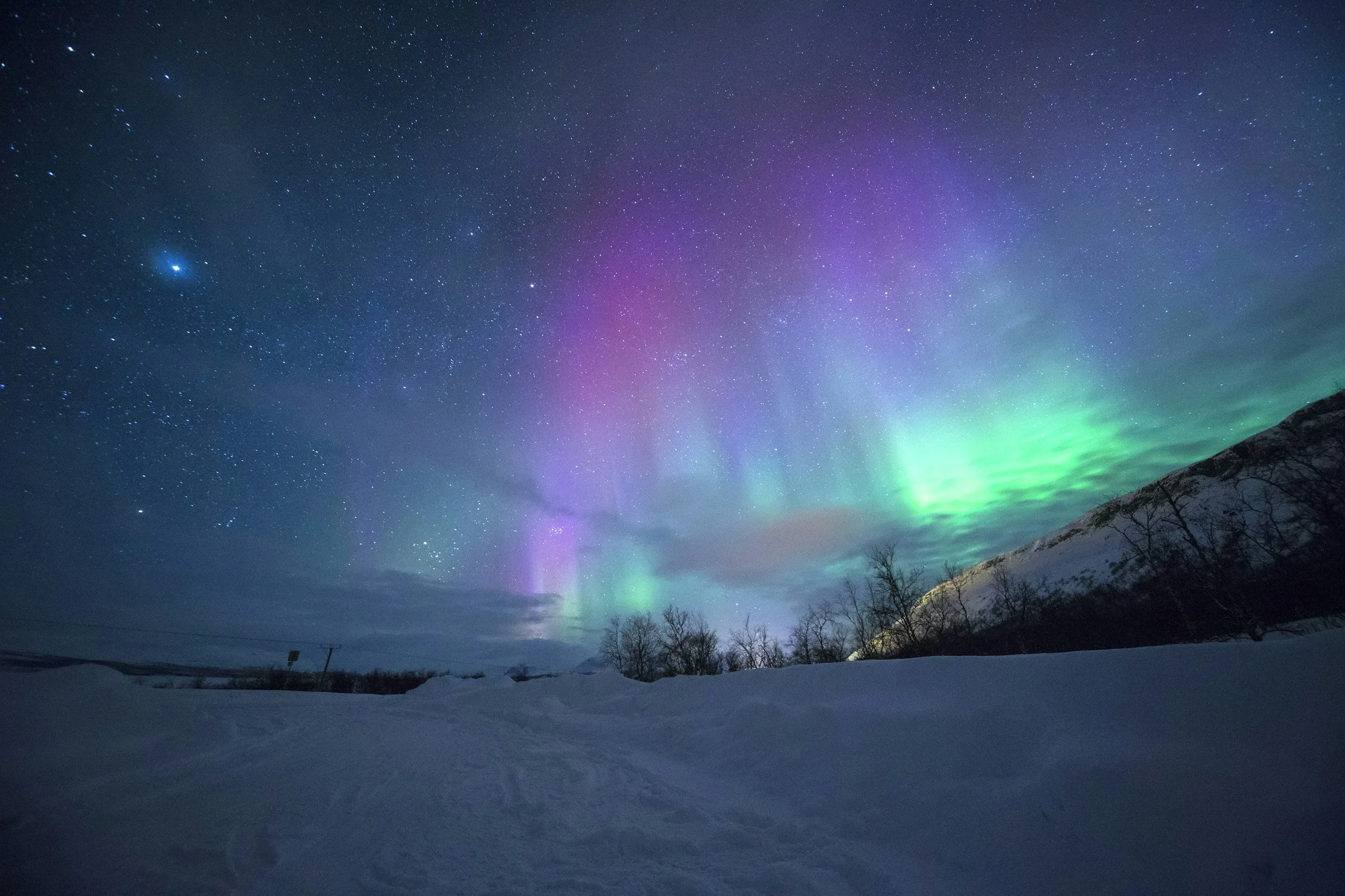 Northern lights over a snowy landscape at night with visible stars in the sky.
