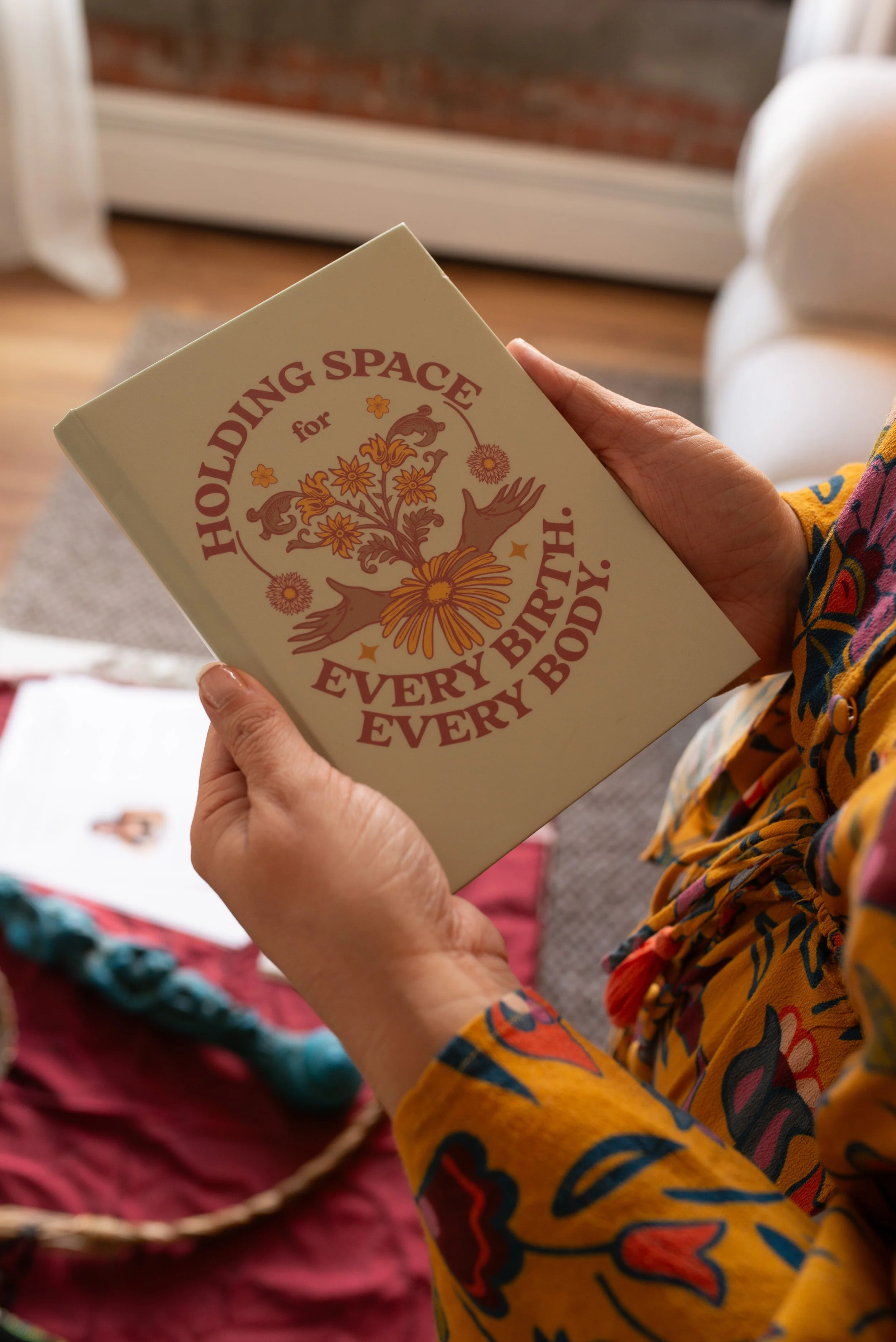 Person holding a book titled "Holding Space for Every Body, Every Birth" with floral and hand illustrations on the cover.