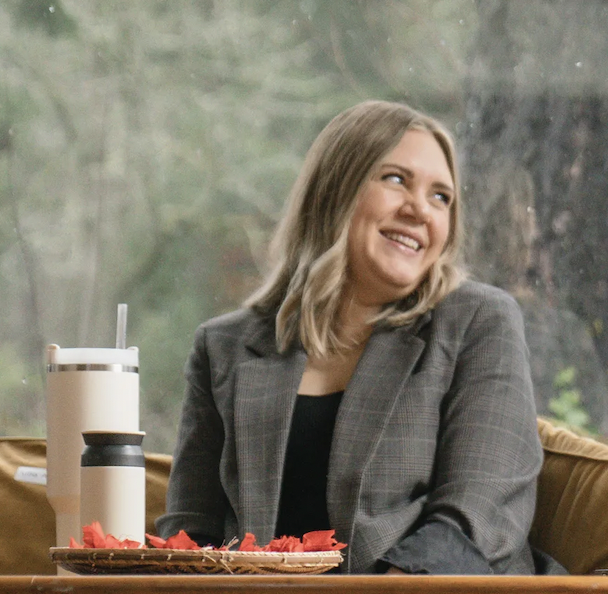 Man sitting on a bench against a beige wall, wearing a blue short-sleeve sweater and beige pants, casting a shadow.