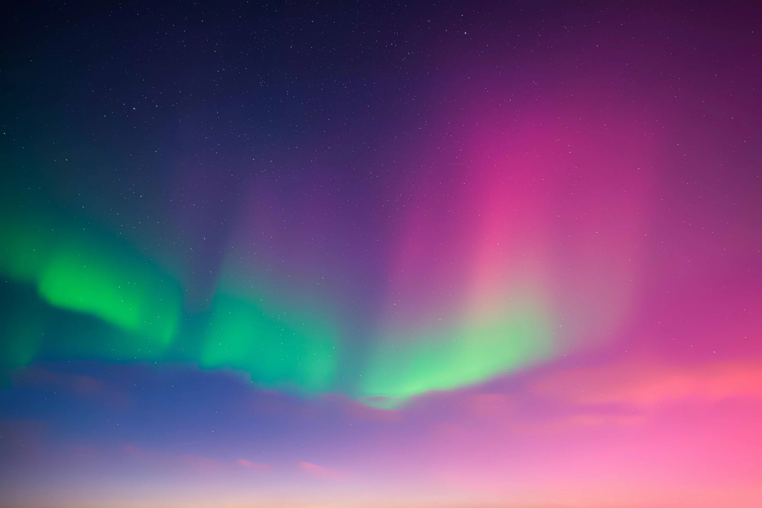 Northern Lights with green and pink hues over a starry night sky.