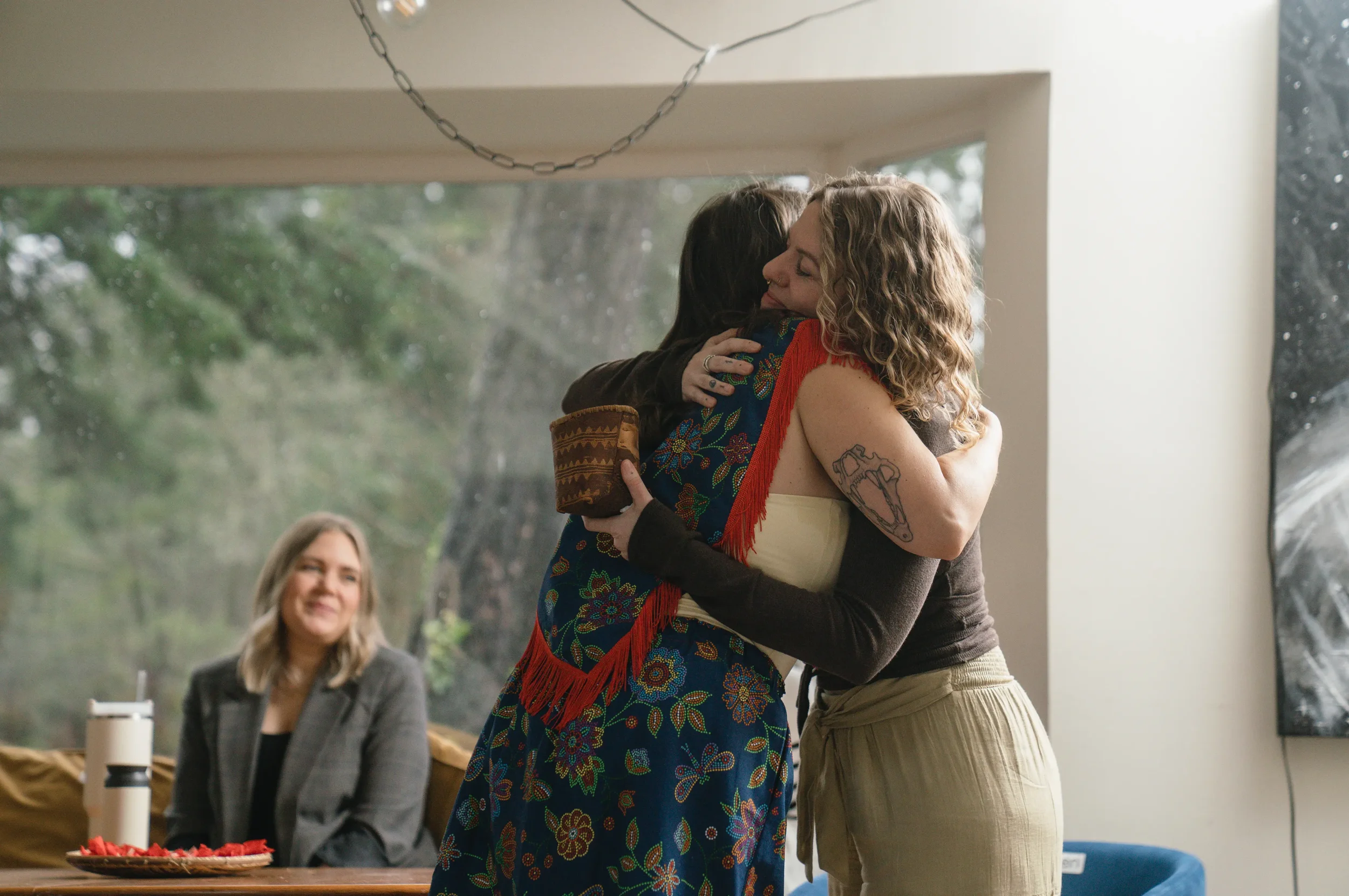 Young woman sitting in an open tent, relaxing in sunlight, wearing a white top, ripped jeans, and a hat, with her eyes closed and her hand on her forehead.