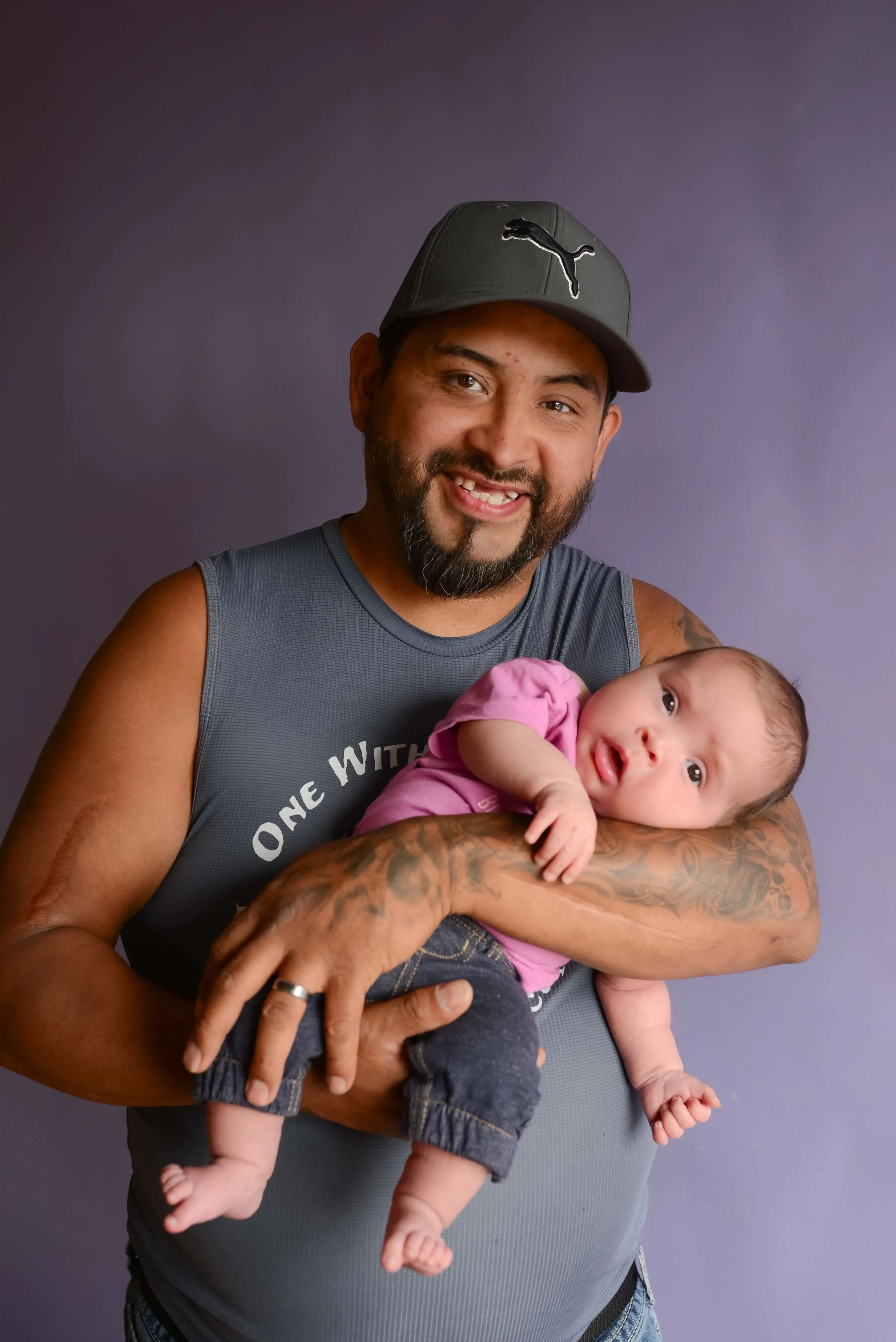 A man holding a baby in his arms, smiling, against a purple background.