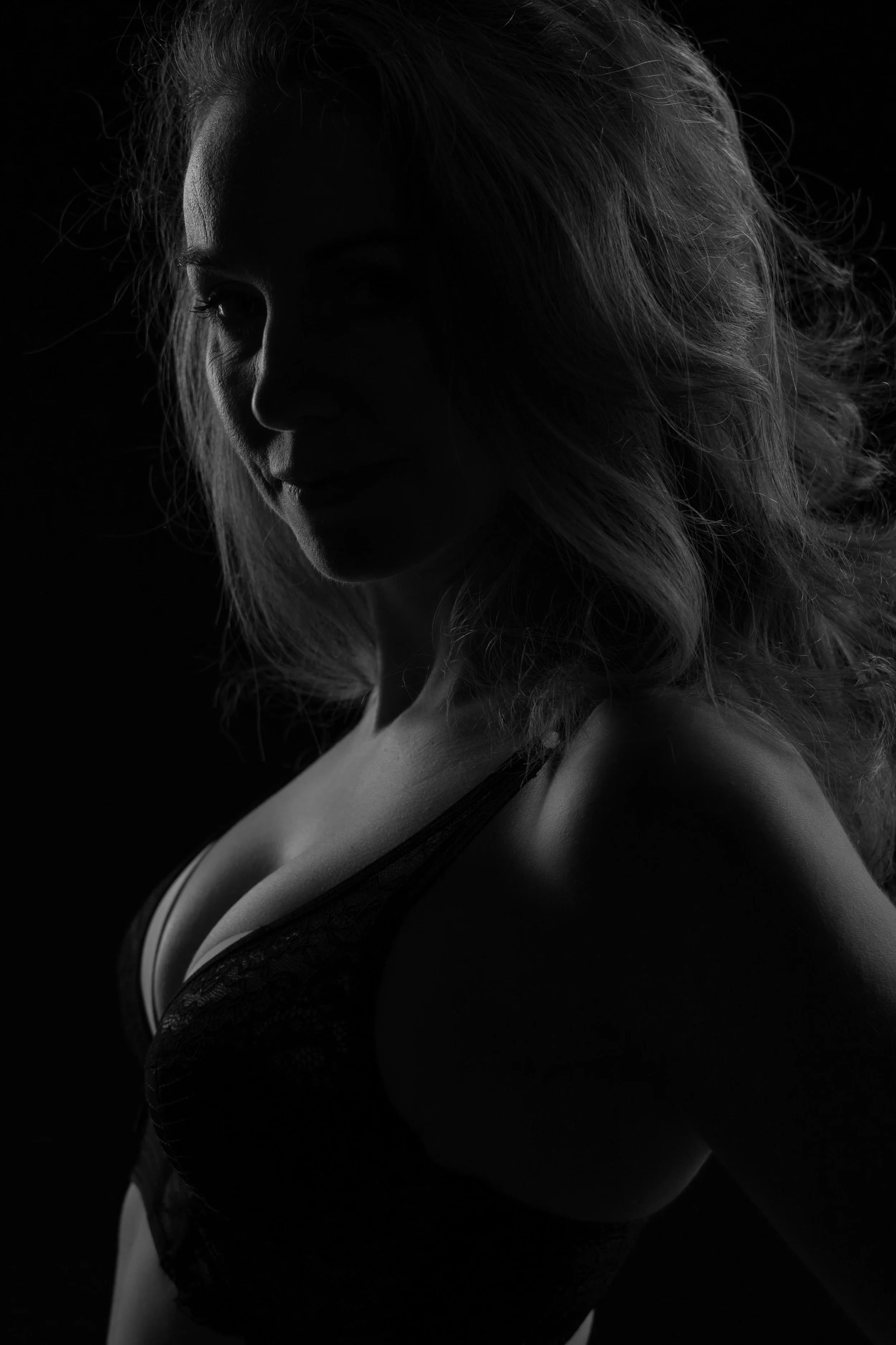 Zwarte en witte foto van een vrouw met golvend haar die in schaduw is gehuld, met alleen haar gezicht en schouders licht.
