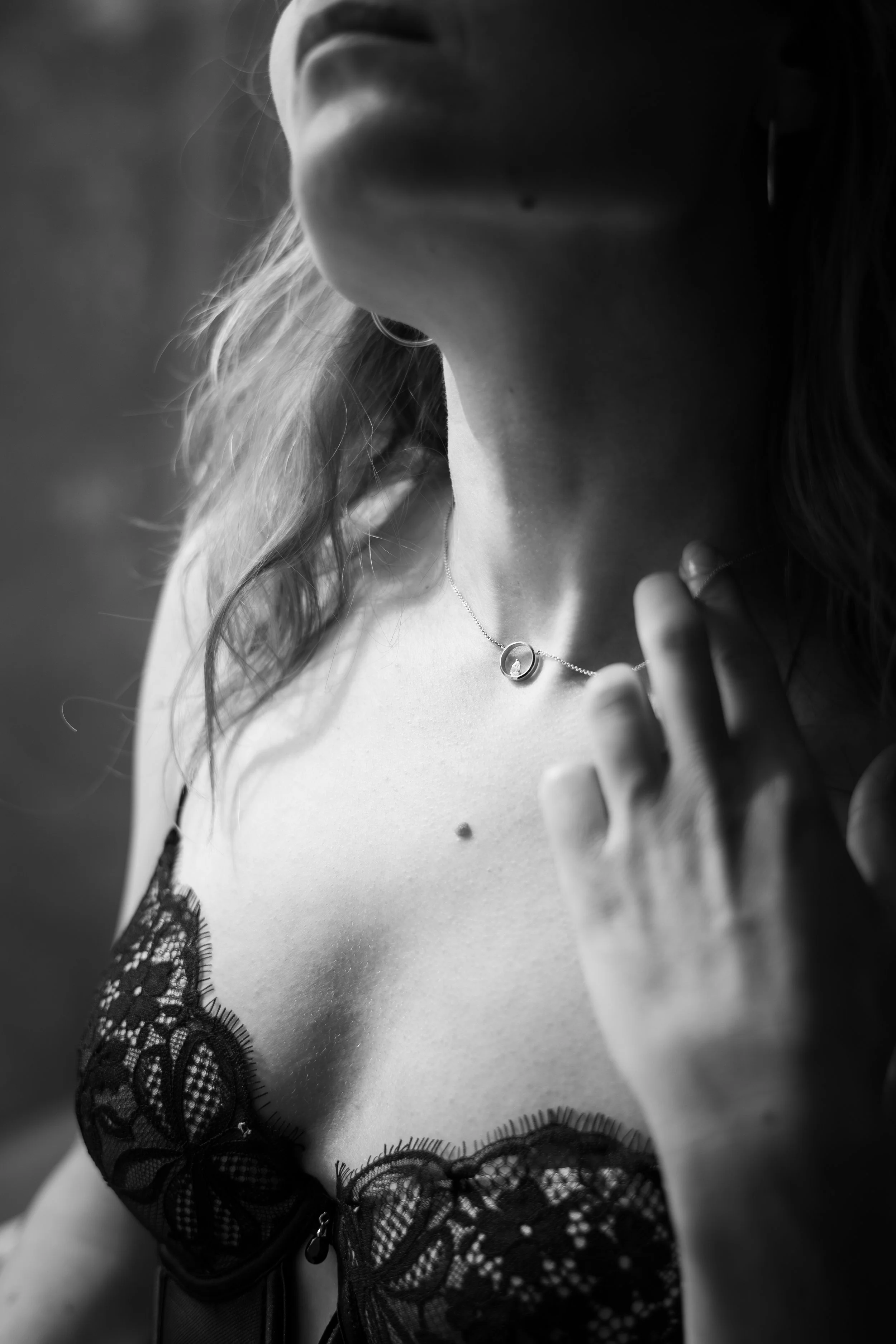 Close-up van een vrouw met donker haar, die een zwart kanten top draagt en een zilveren ketting met een cirkelvormige hanger draagt.