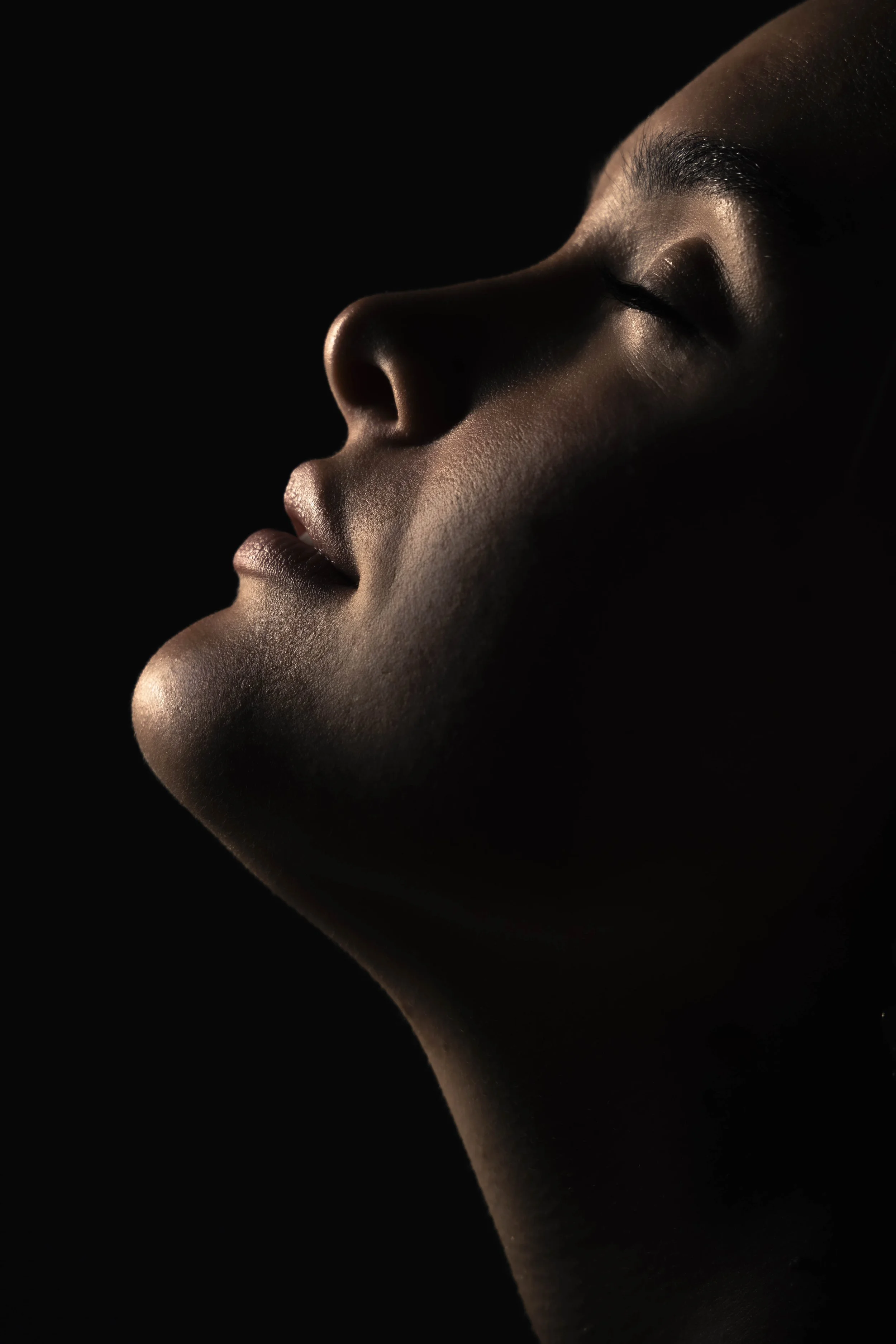 Close-up van een vrouw met gesloten ogen, licht op haar gezicht tegen een donkere achtergrond.