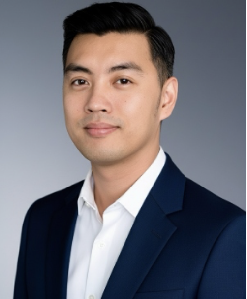 Professional headshot of a young man in a dark blue suit and white shirt, smiling softly against a gray background.