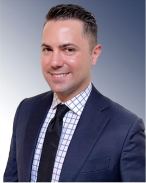 Professional portrait of a man in a navy suit, white checked shirt, and black tie, smiling against a gradient background.