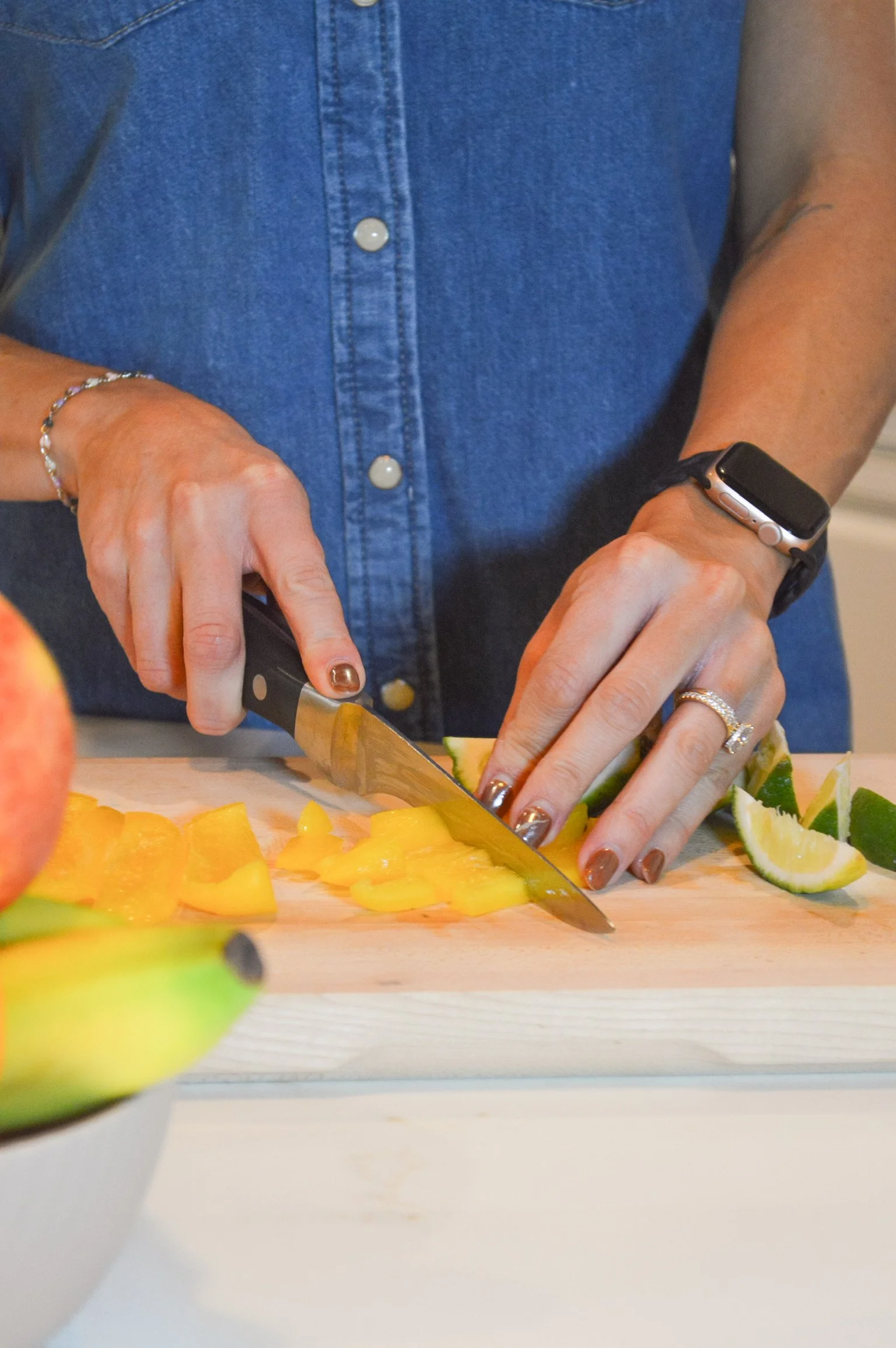 A person chopping yellow mango and lime on a wooden cutting board.