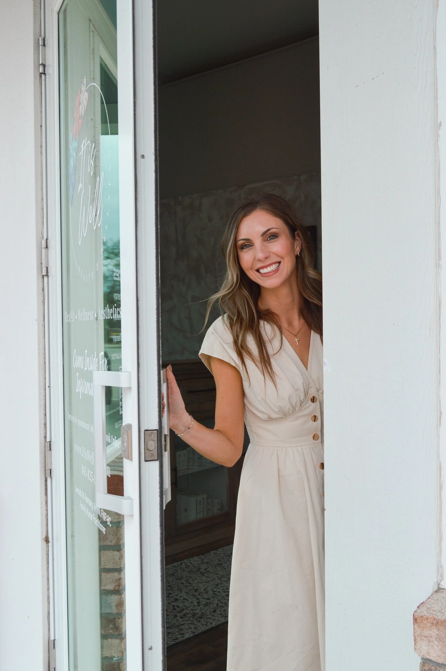 A woman smiling and standing at an open door of a wellness or aesthetic clinic.